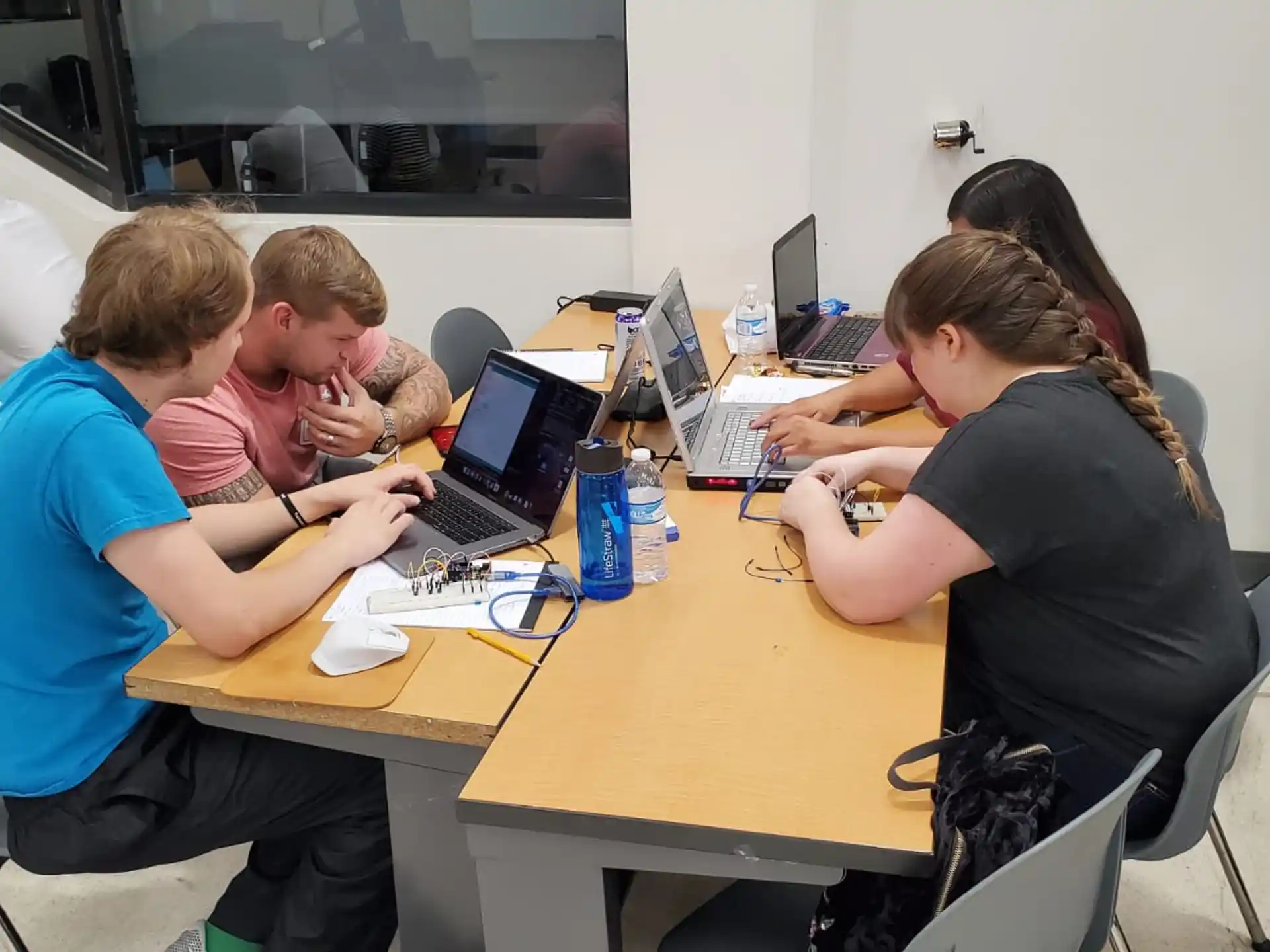 a group of people sitting around a table with laptops