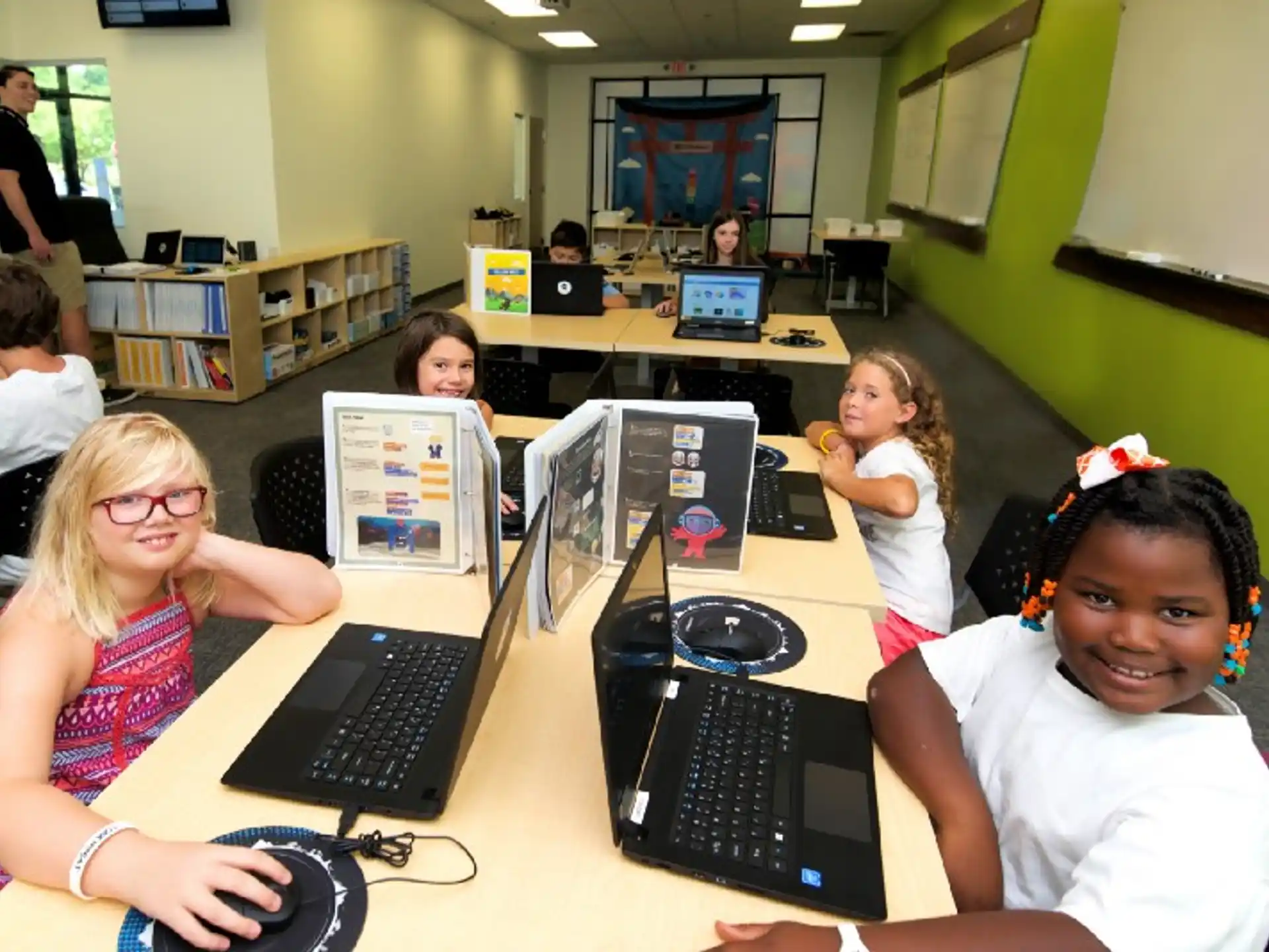 a group of children sitting at a table with laptops