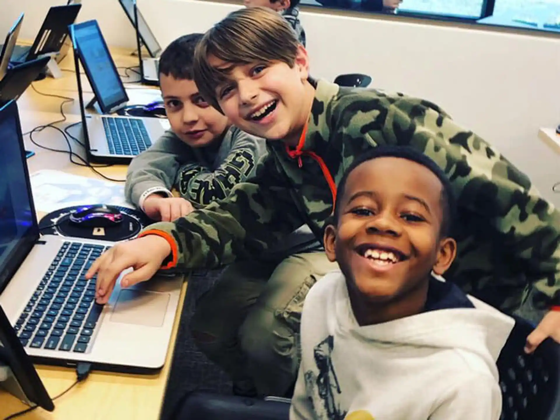 a group of boys smiling and sitting at a desk with laptops
