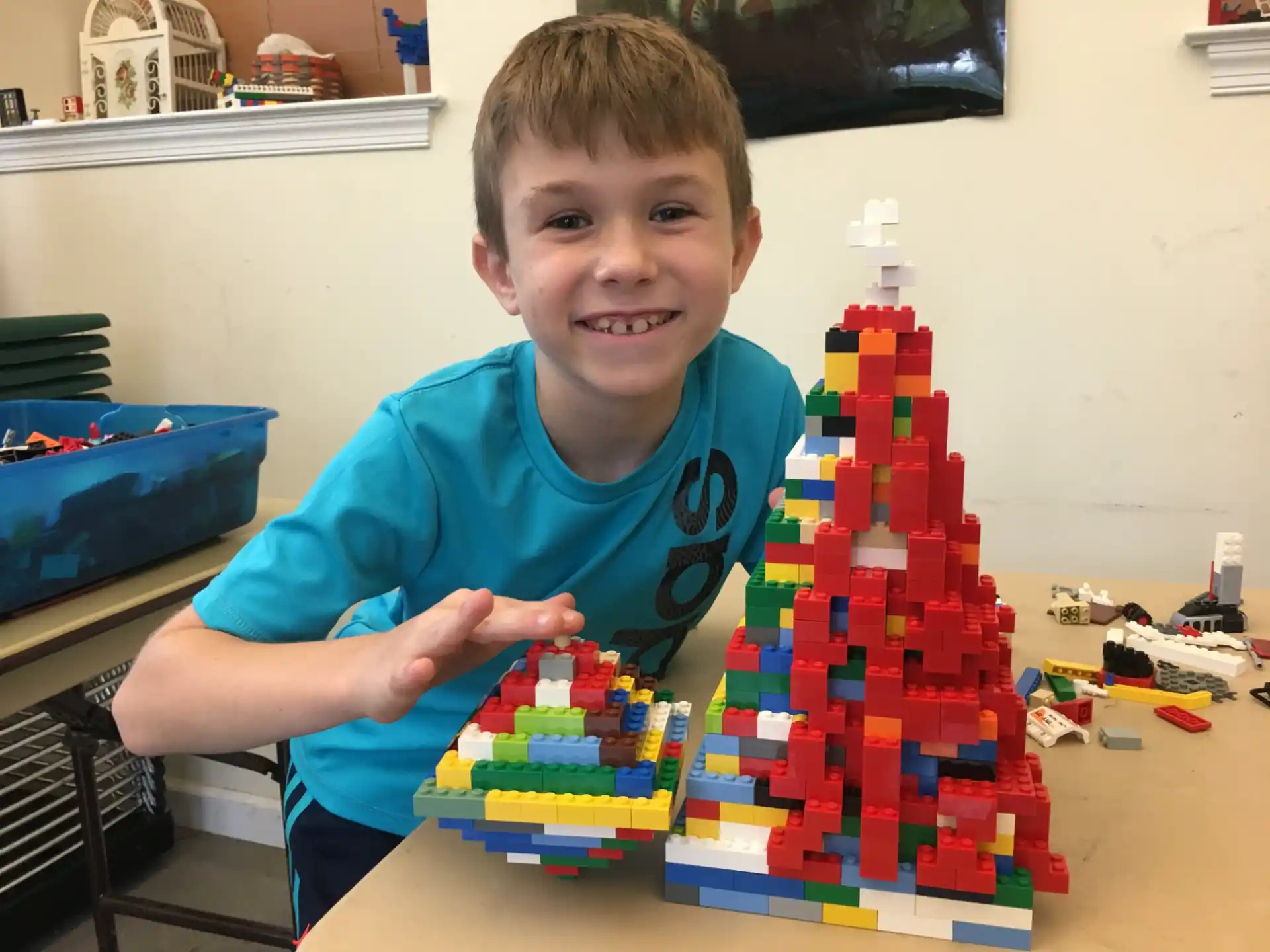 a boy smiling with a building made of building blocks
