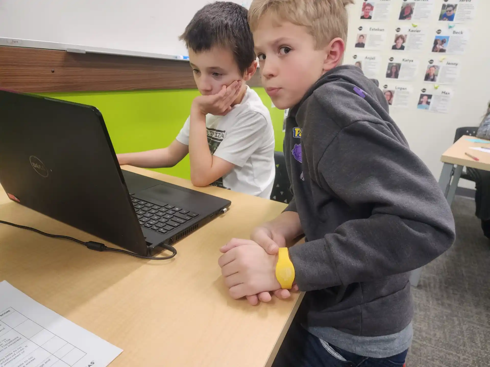 a couple of boys sitting at a table with a laptop