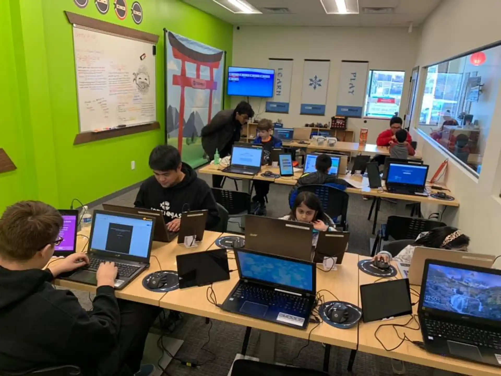 a group of people working on laptops in a room with green walls