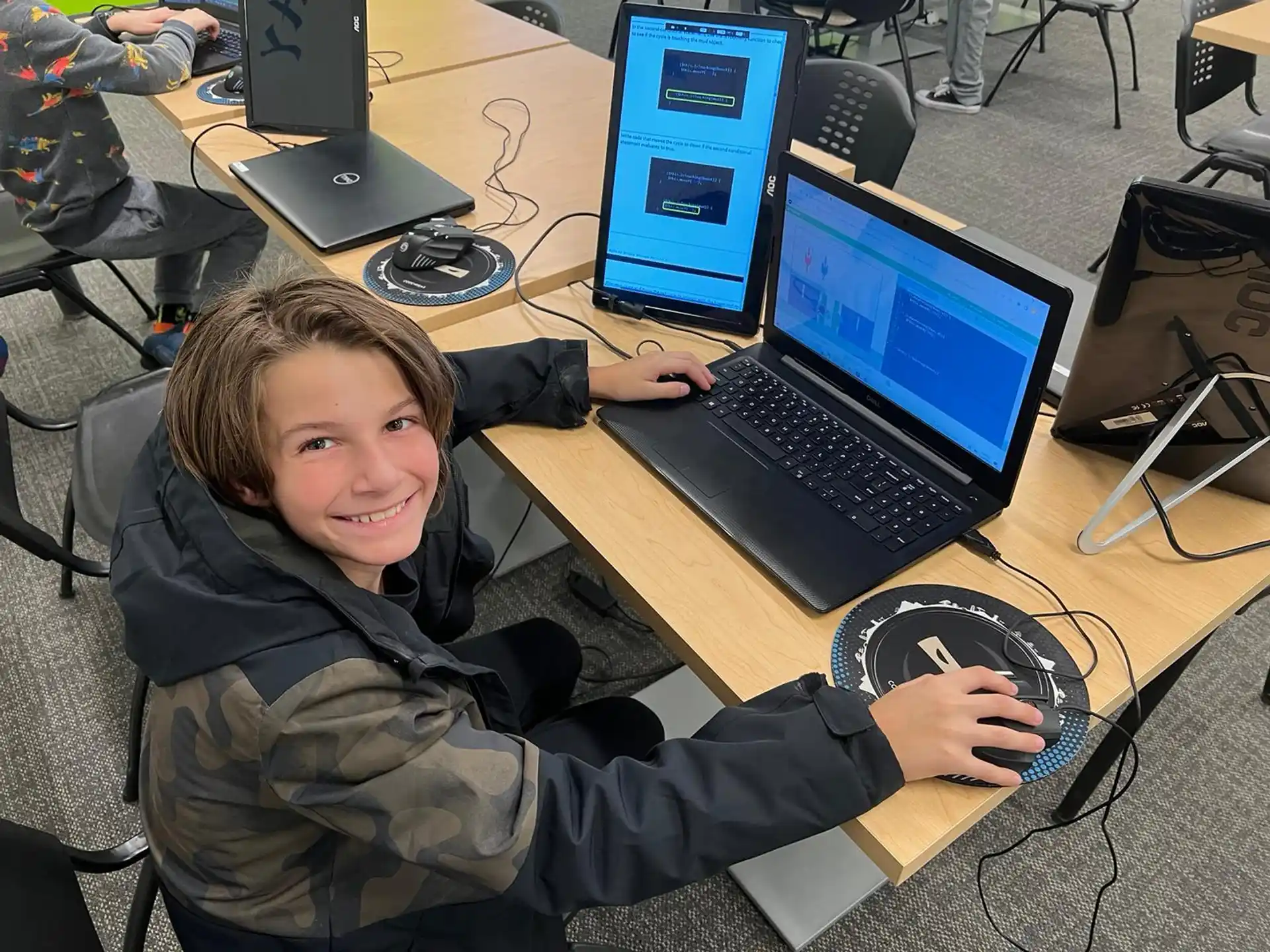 a boy sitting at a desk with a laptop and mouse