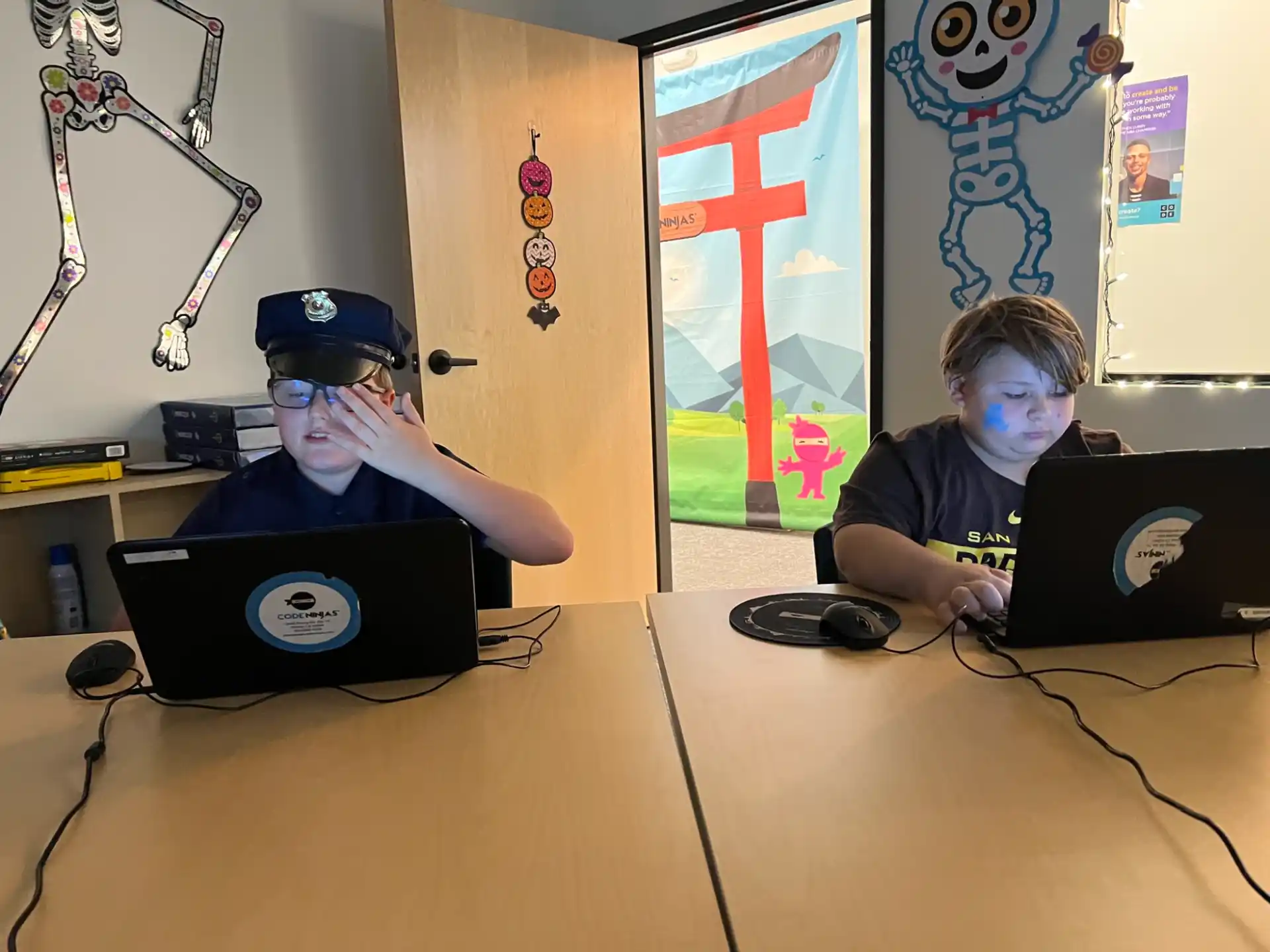 a couple of boys sitting at a table with laptops