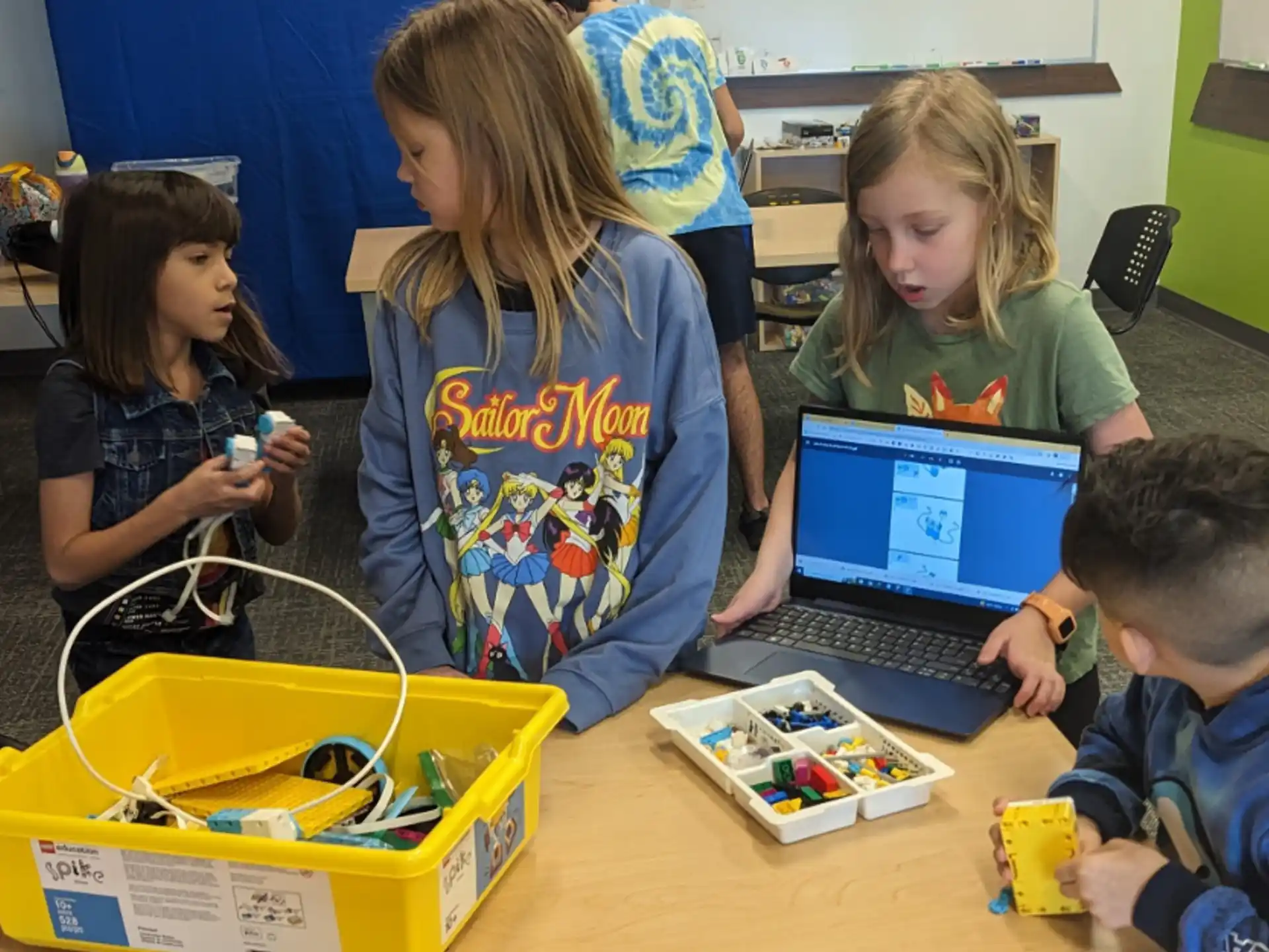 a group of children sitting at a table looking at a laptop