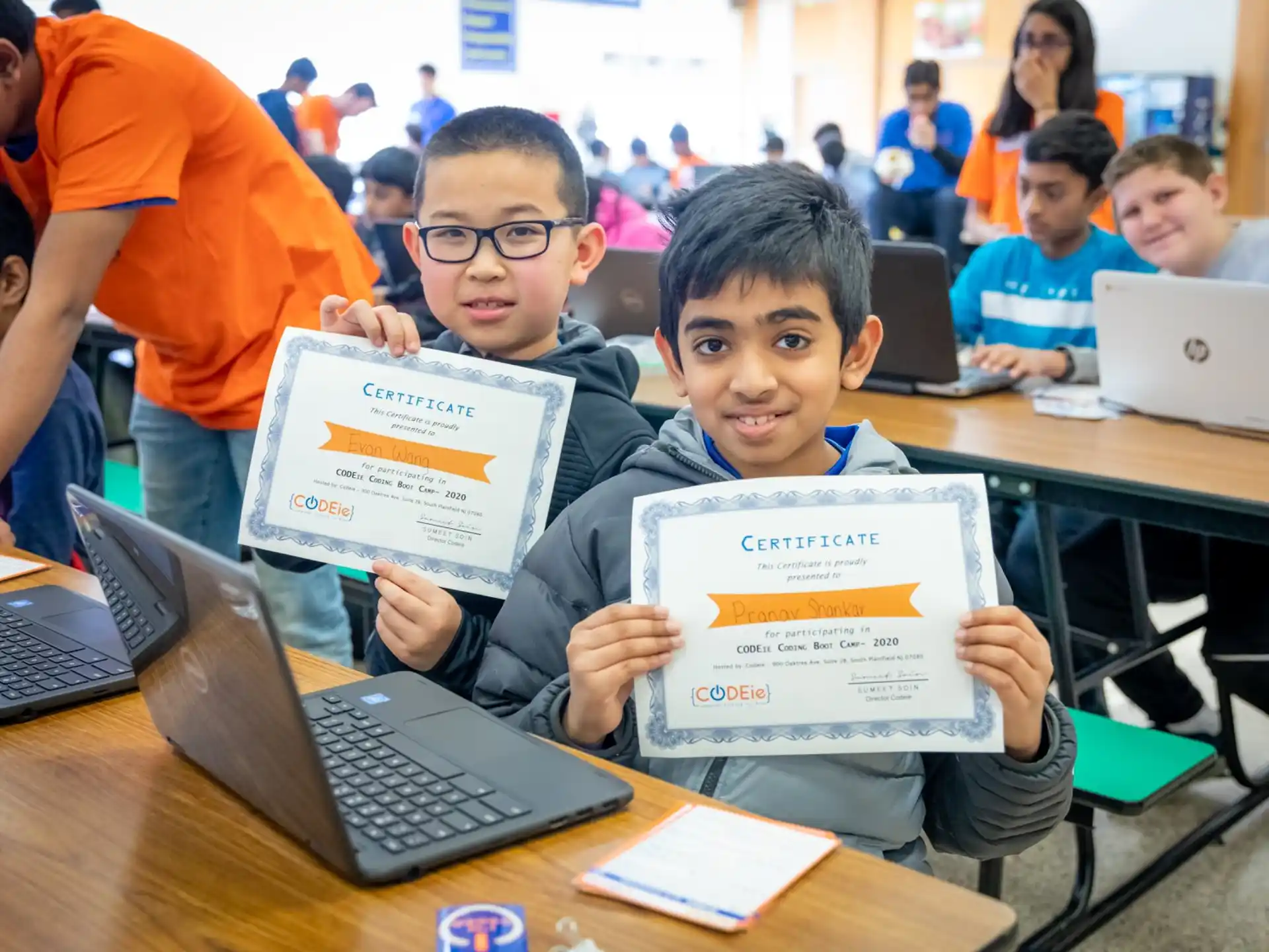 a group of boys sitting at desks with laptops and papers
