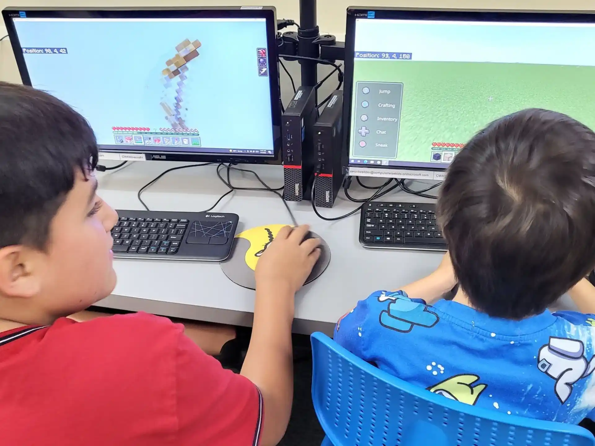 a couple of boys sitting at a desk with computers