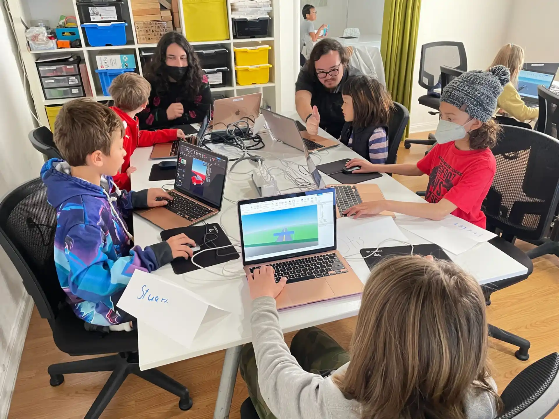 a group of people sitting around a table with laptops