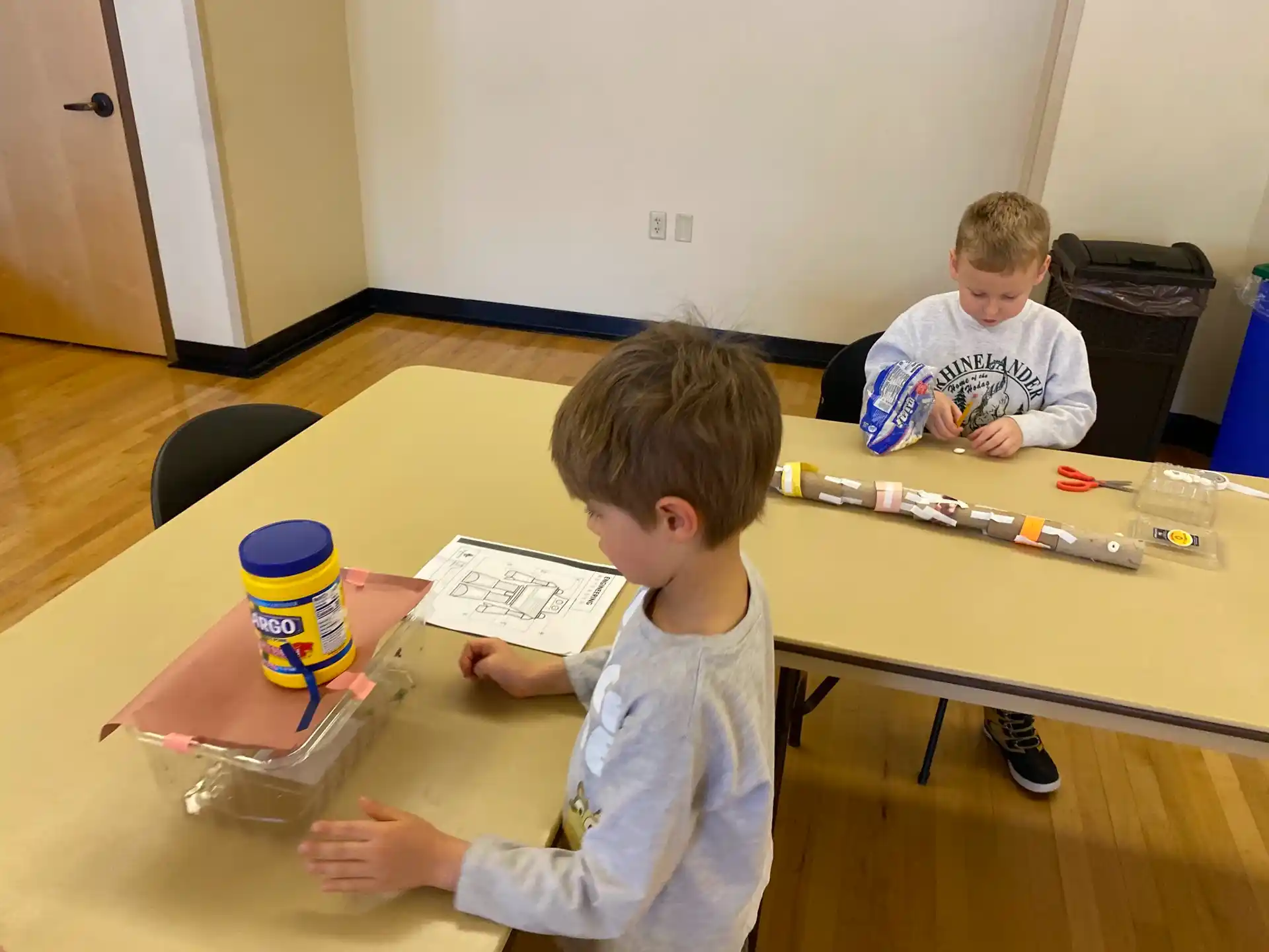 a couple of boys sitting at a table with a paper and pencils