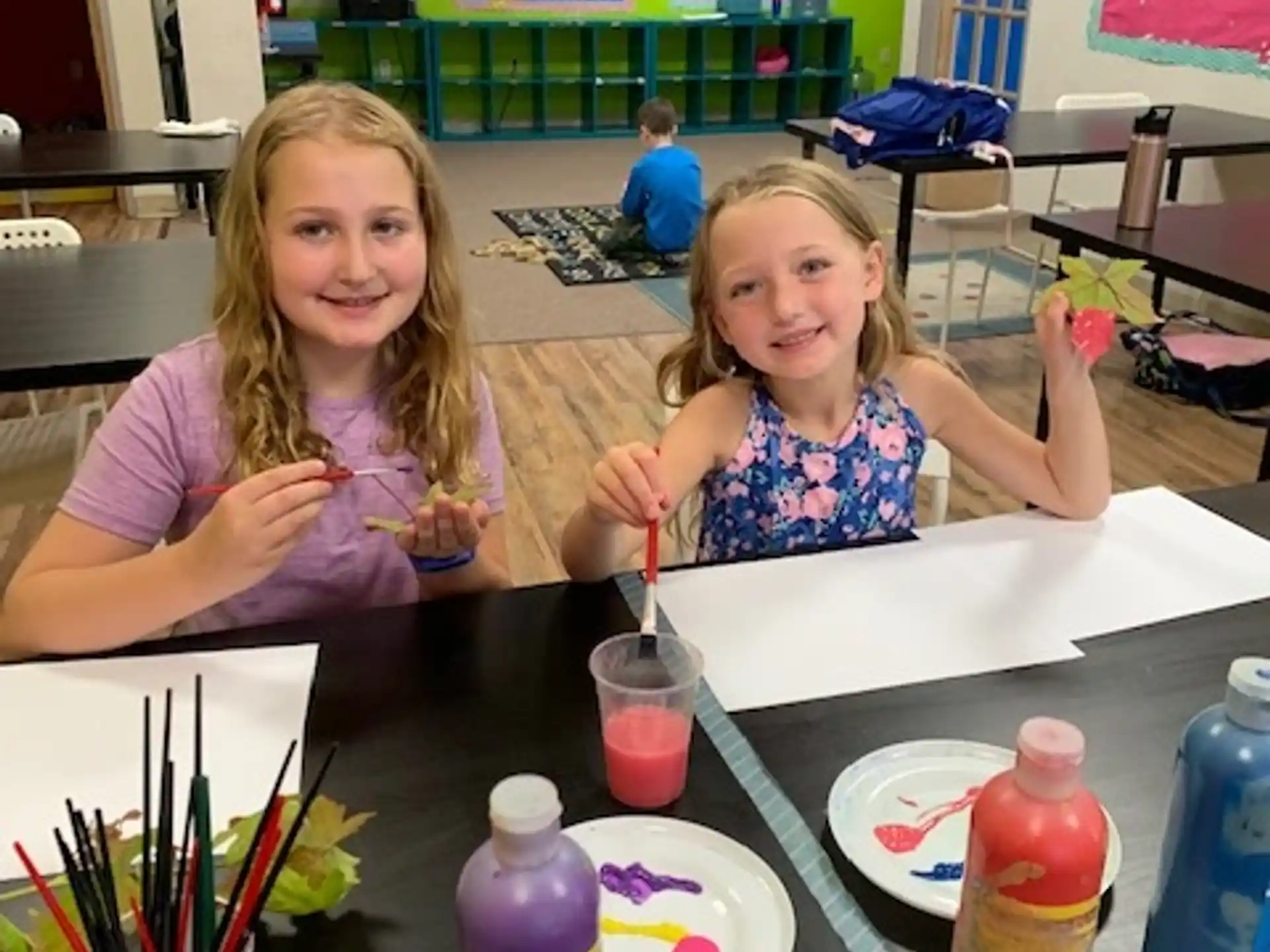 a couple of girls sitting at a table with food and drinks