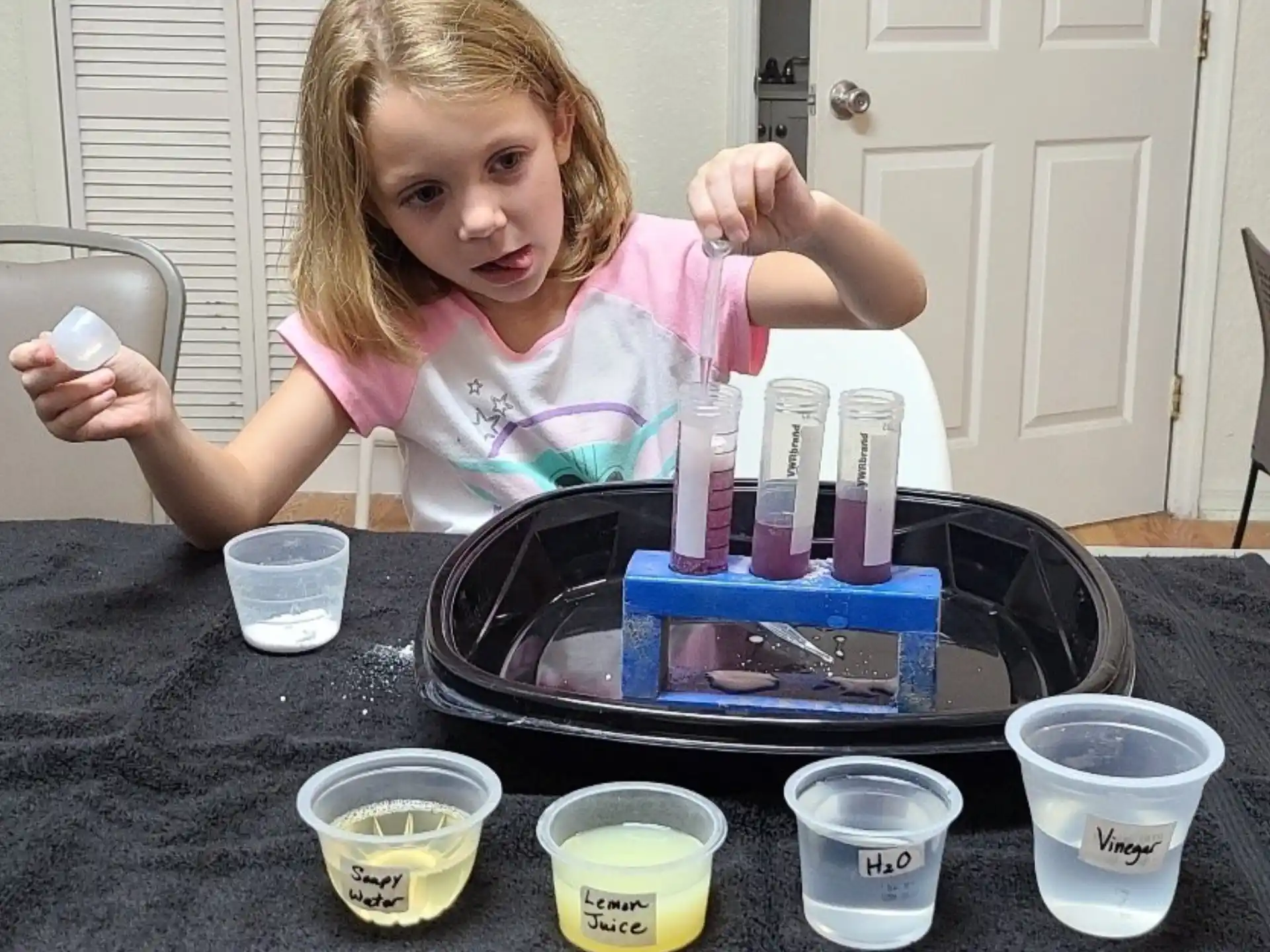 a girl sitting at a table with a tray of paints and a container of paint