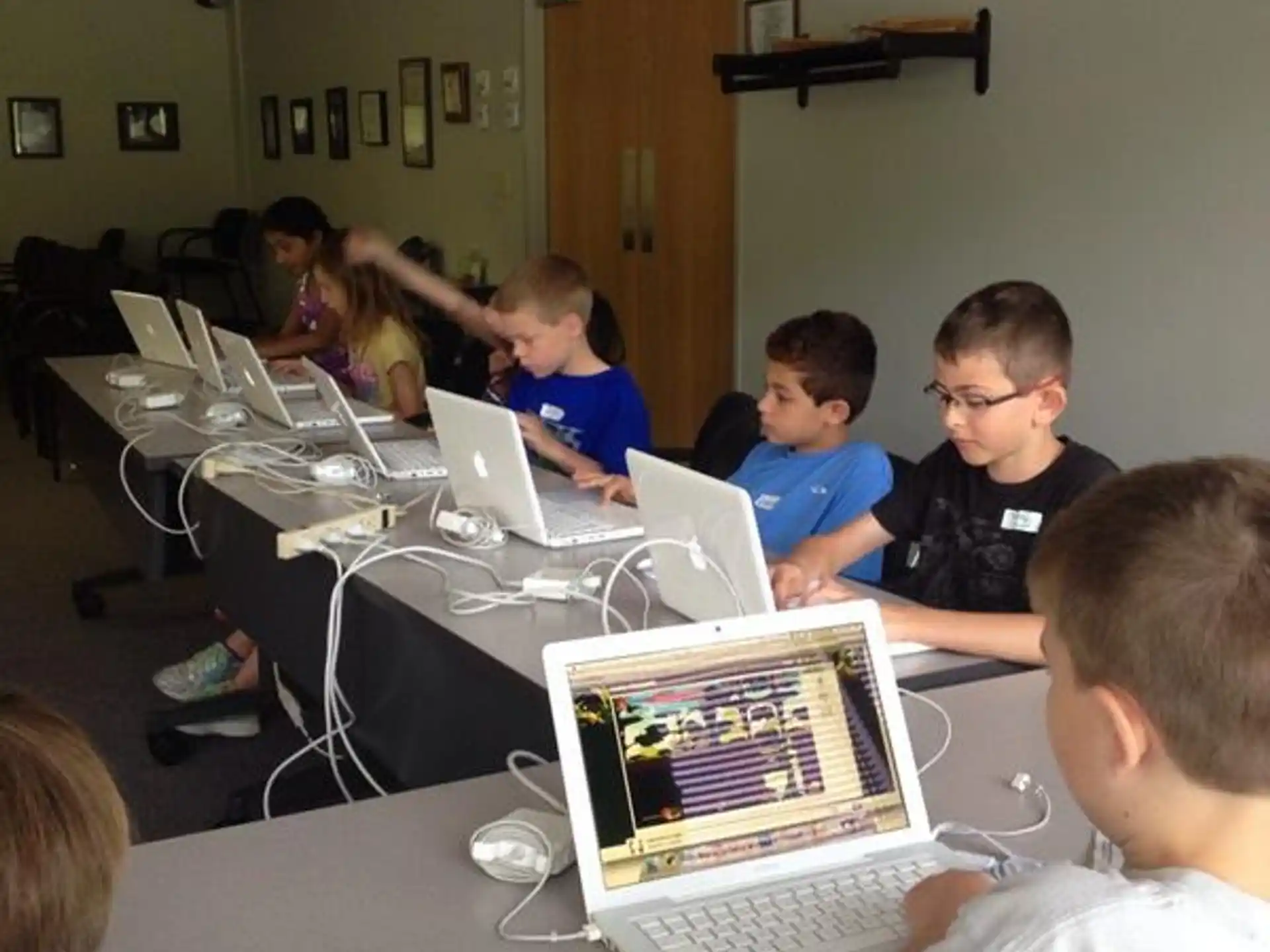 a group of kids sitting at a table with laptops