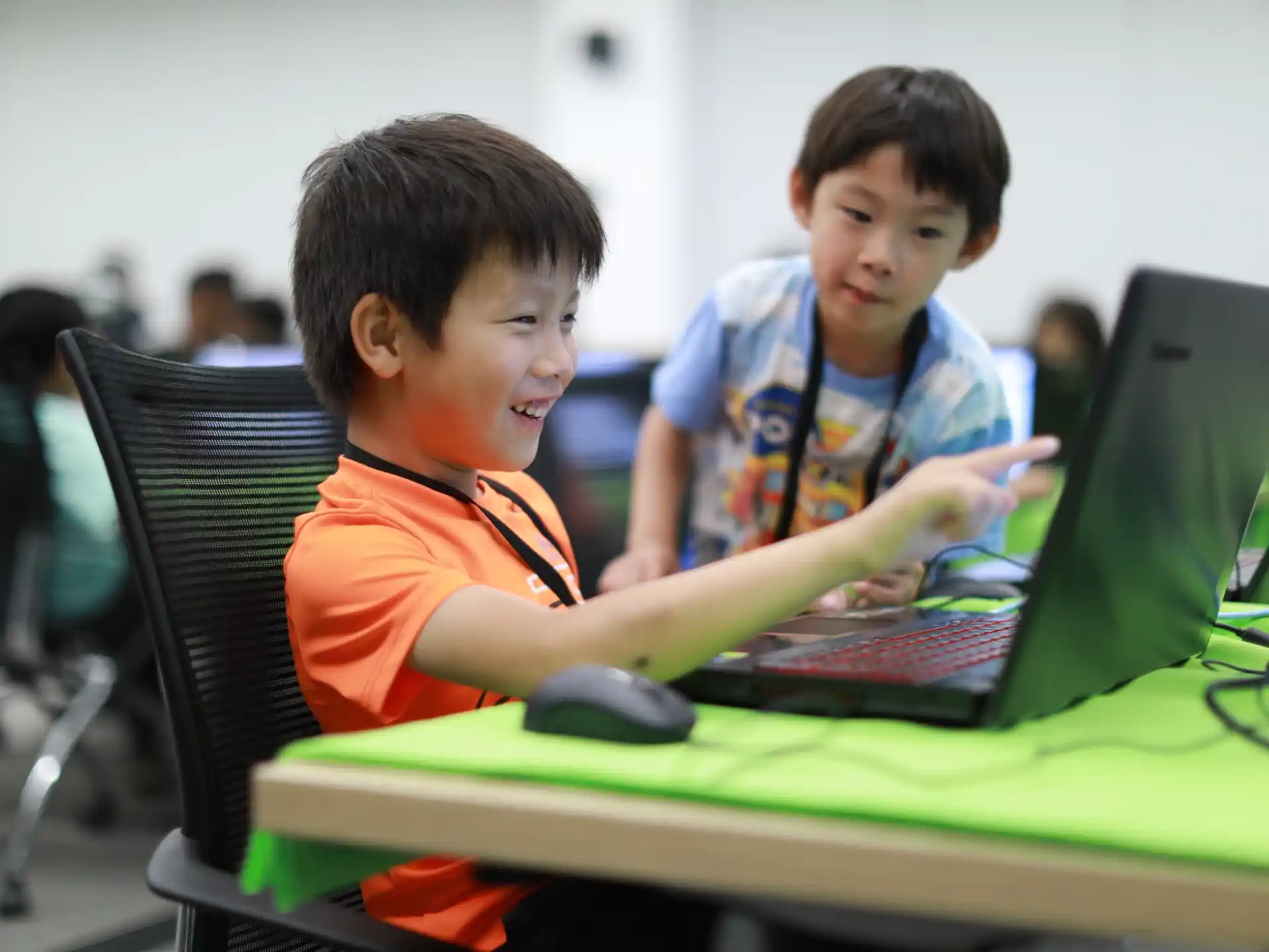 a couple of boys sitting at a table with a laptop