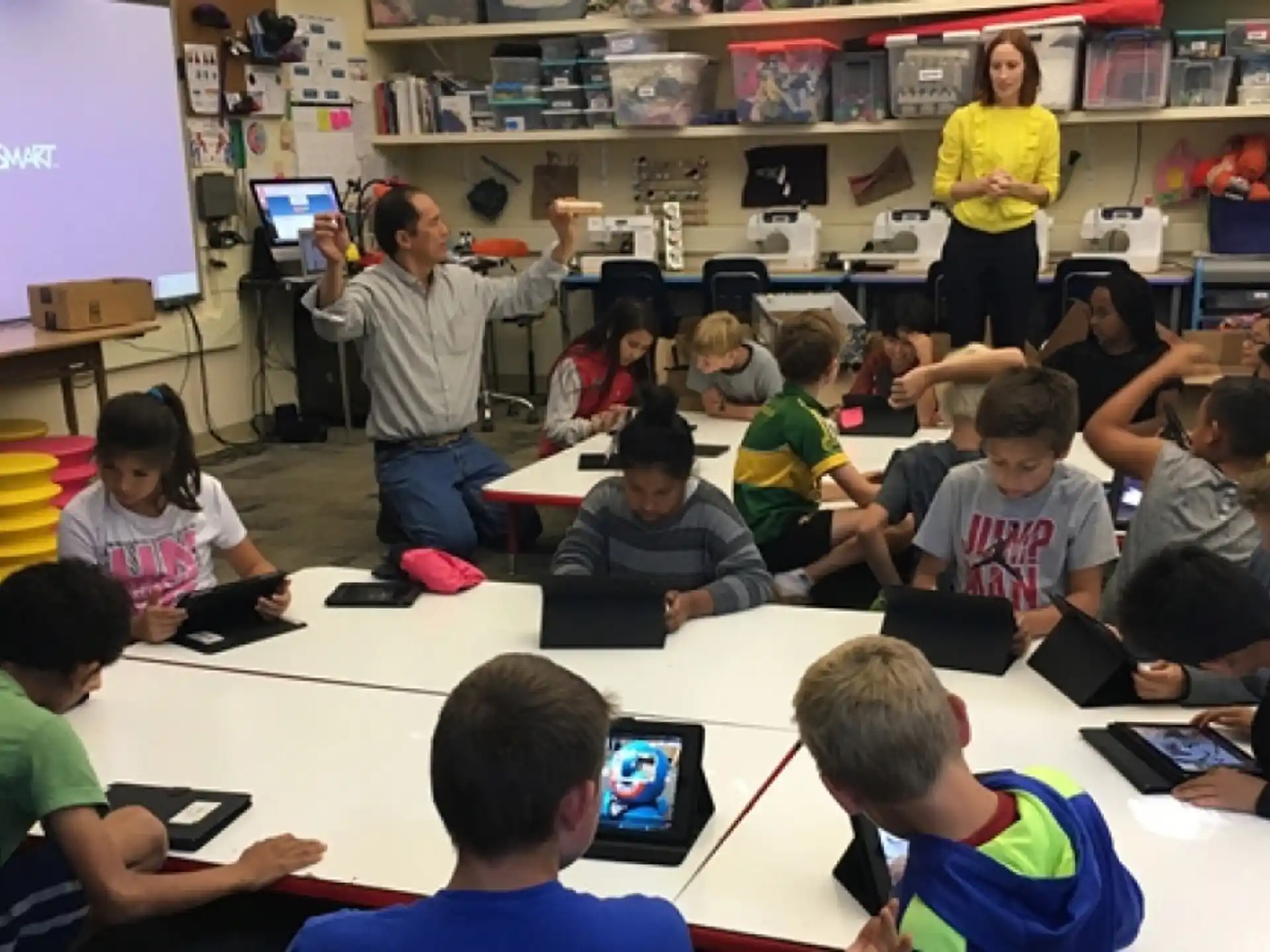 a group of children sitting at a table with computers