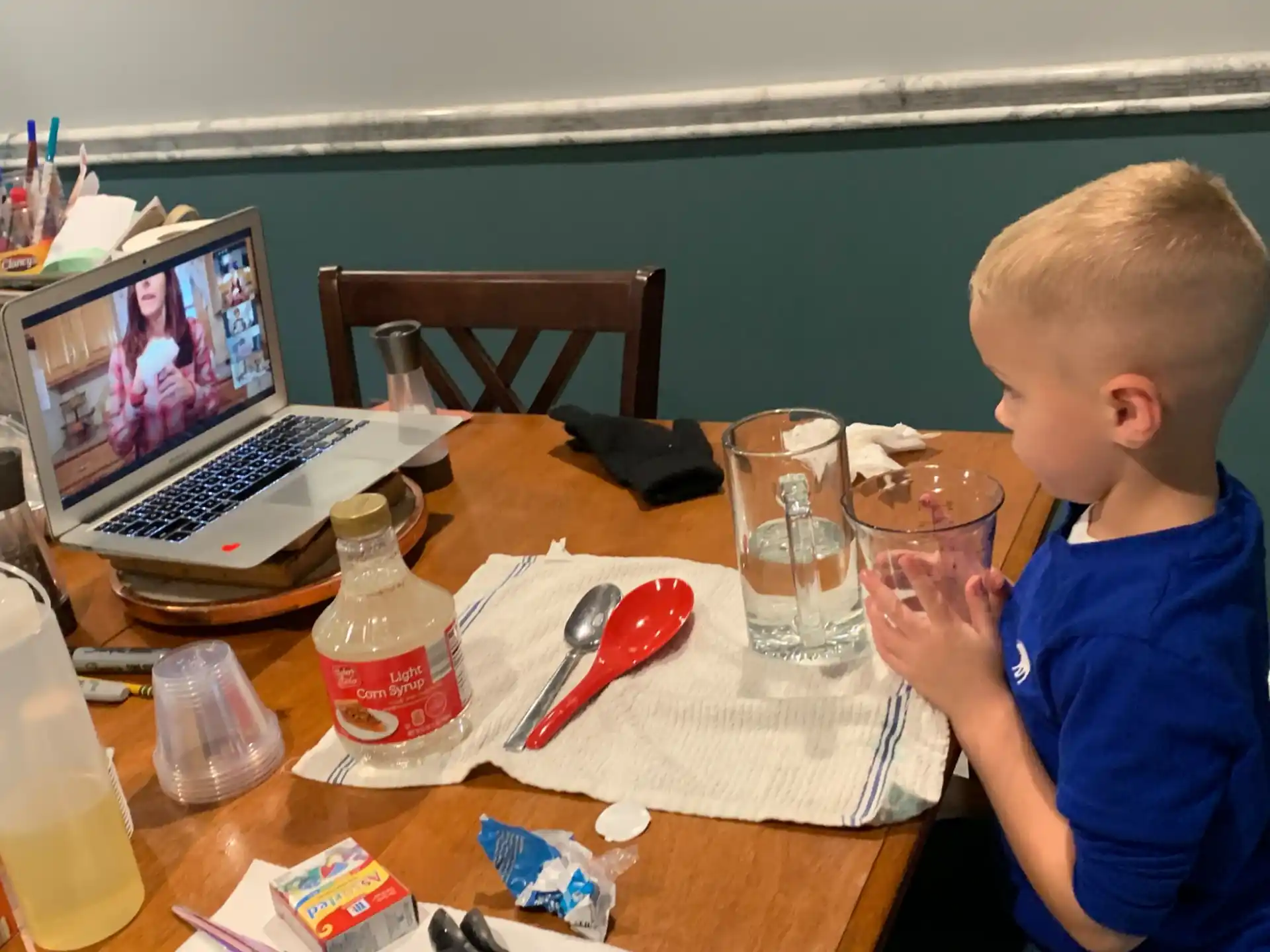 a kid sits at a table with a laptop and a glass of juice