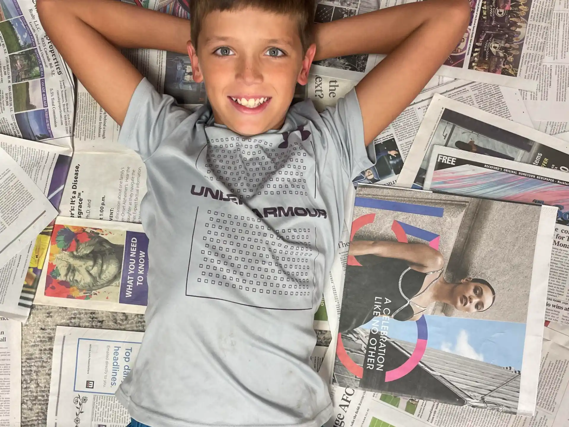 a boy standing in front of a pile of magazines