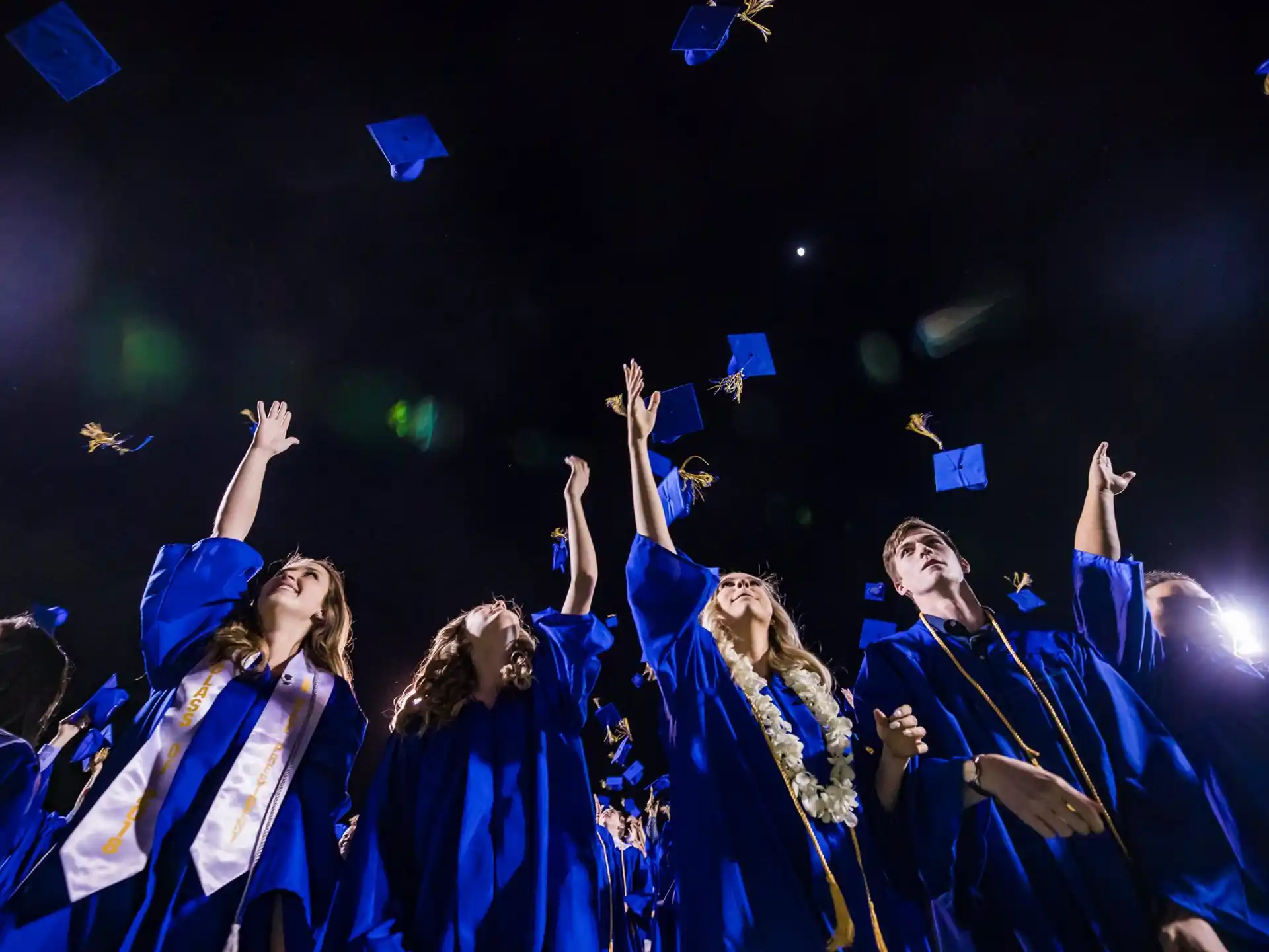 a group of people in blue graduation gowns with their hands up