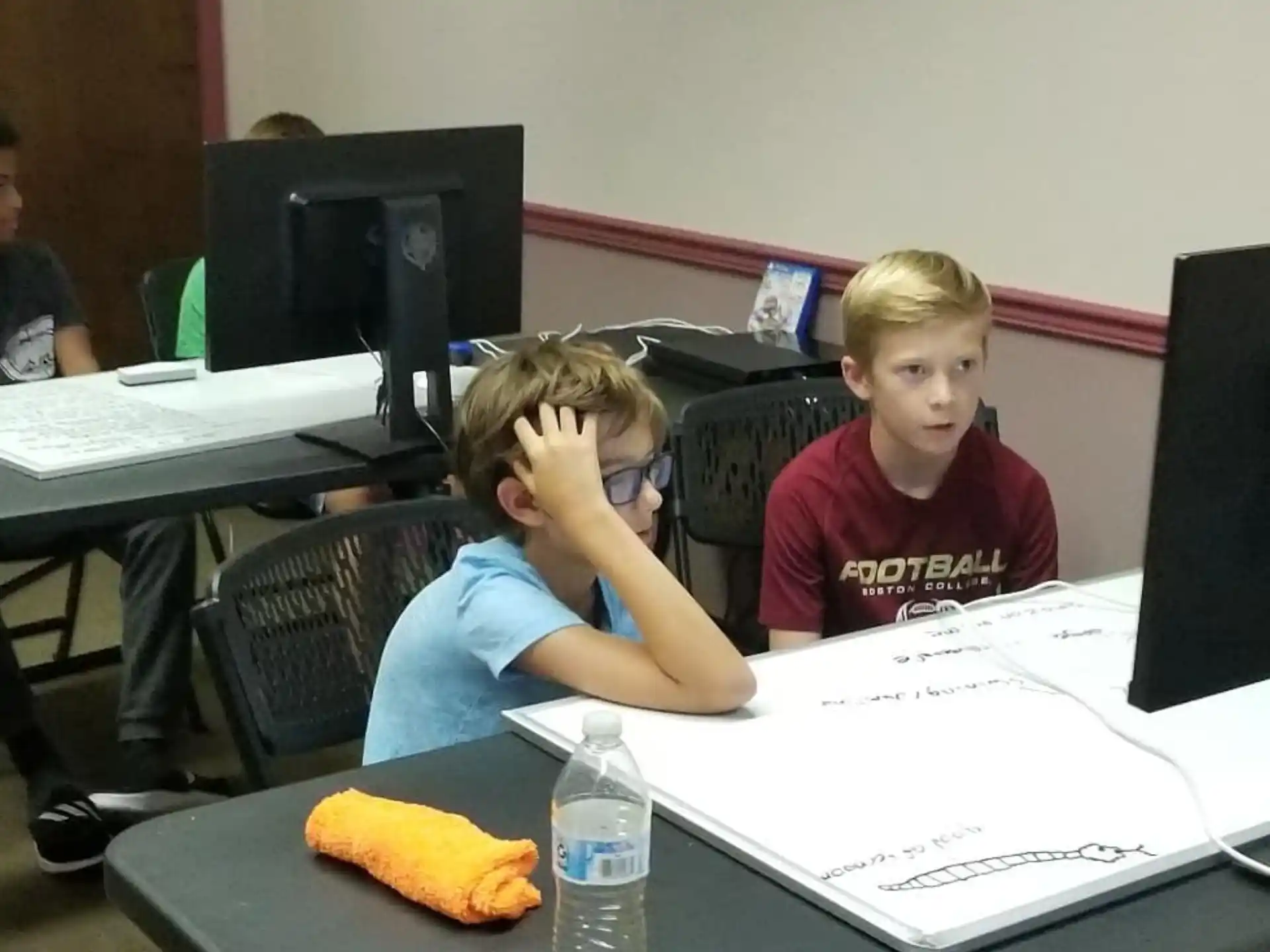 a couple of boys sitting at a table with papers and a water bottle