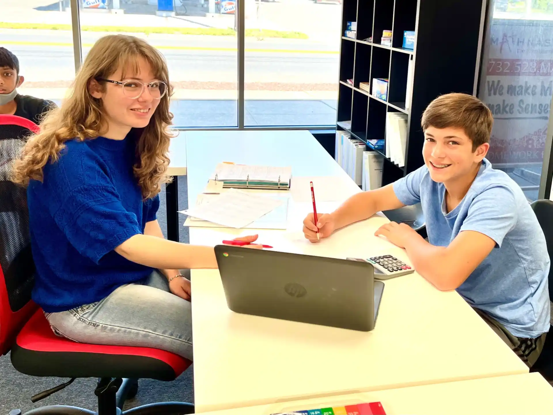 a boy and girl sitting at a table with a laptop