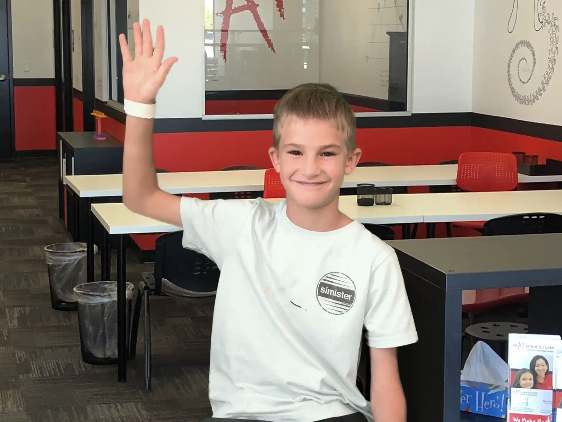 a boy sitting at a desk with his hand up