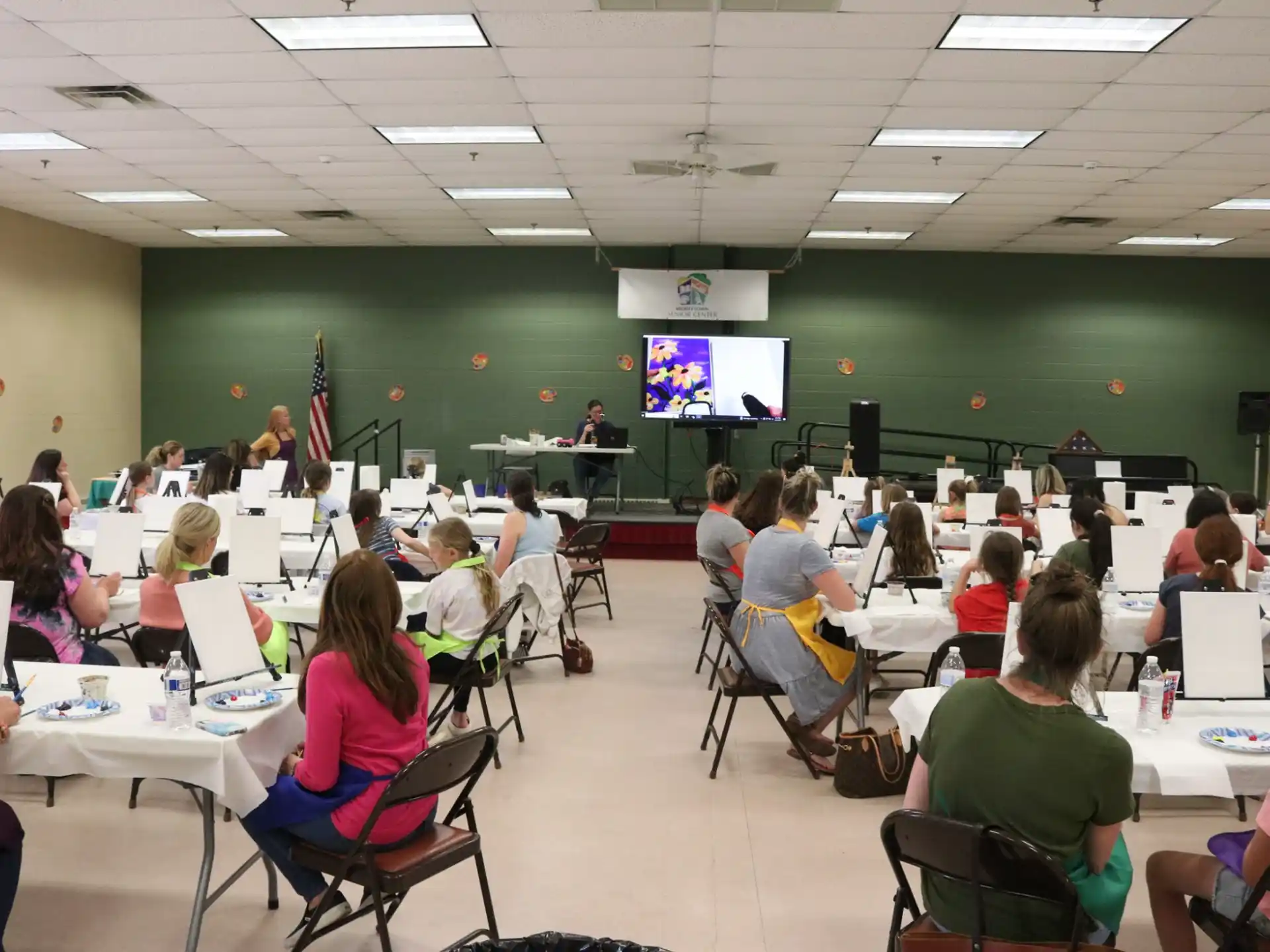 a group of people sitting at tables in a room with a screen