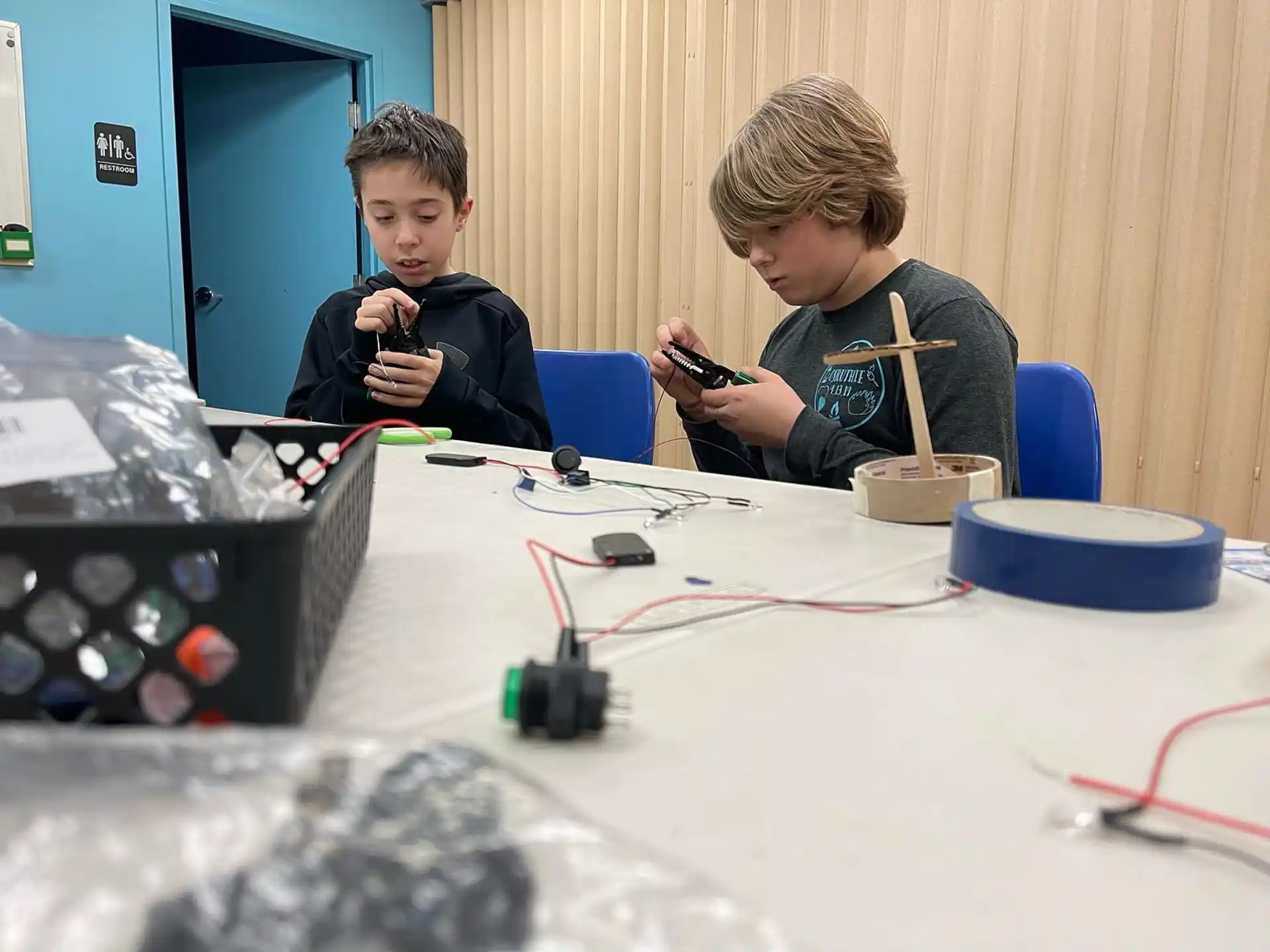 a couple of boys sitting at a table with a white table and wires
