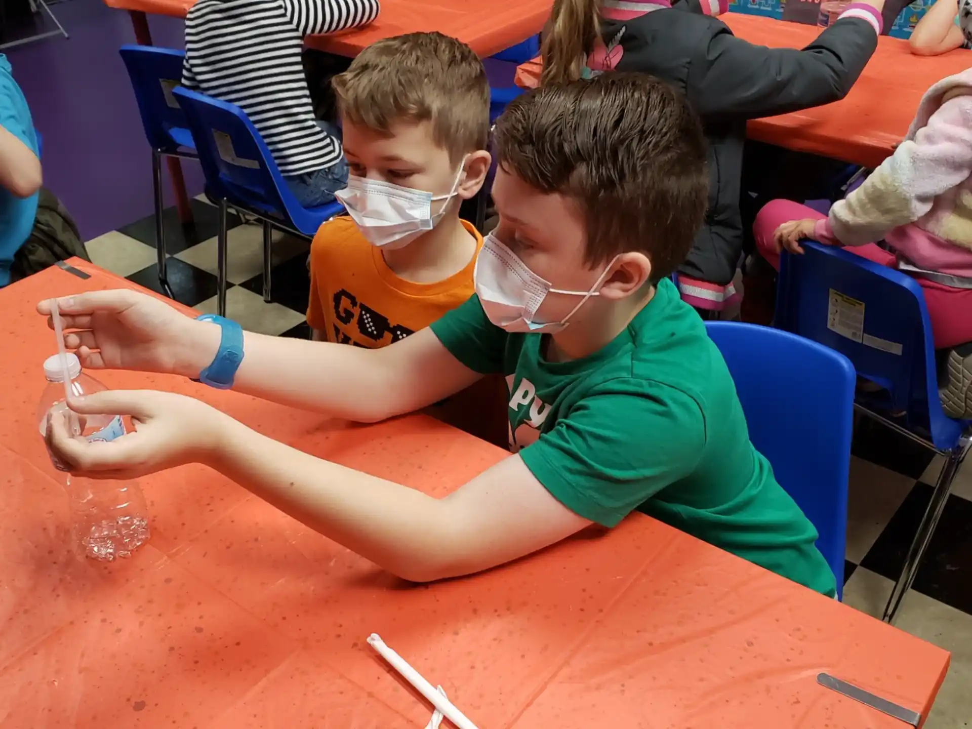 a couple of boys sitting at a table with a marker and a pencil