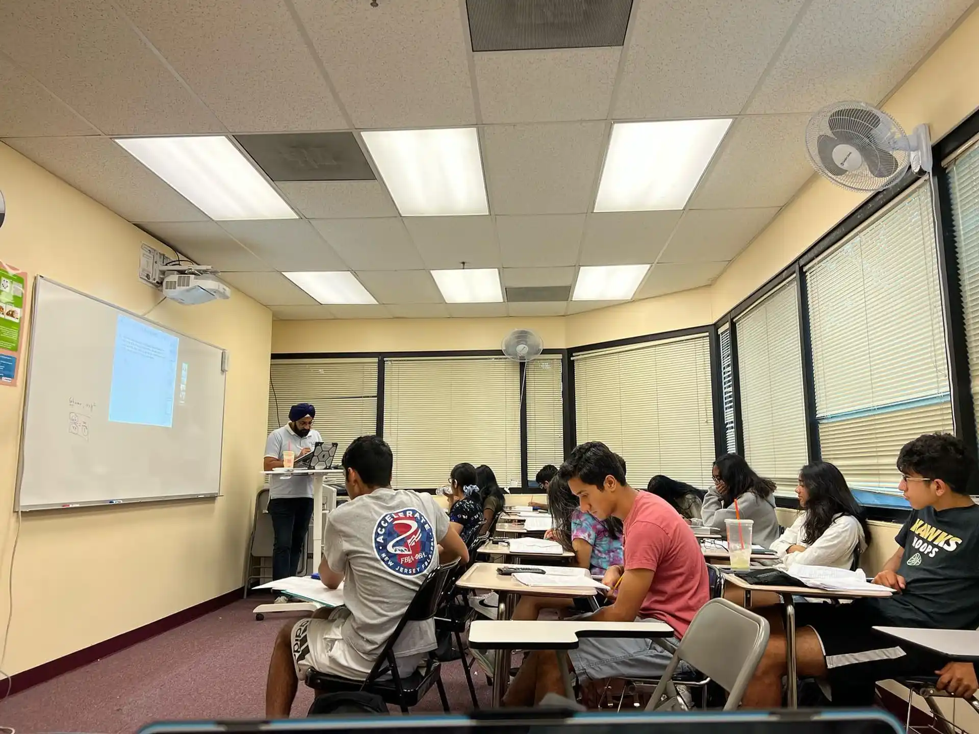a group of people sitting at tables in a room with a projector screen