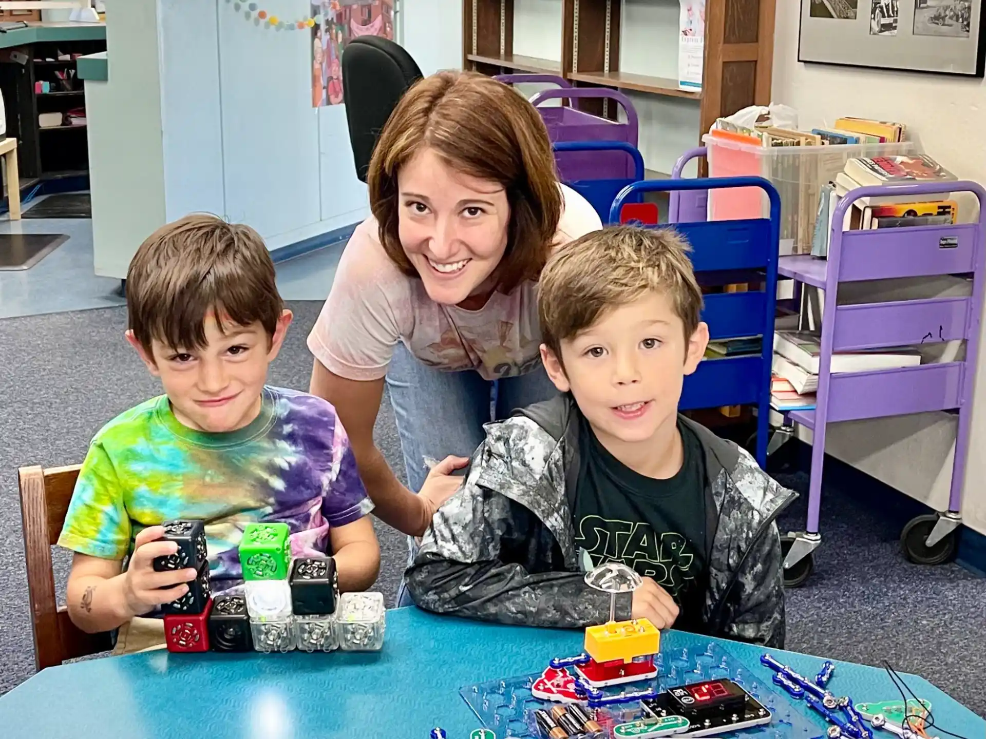 a person and two boys sitting at a table with toys
