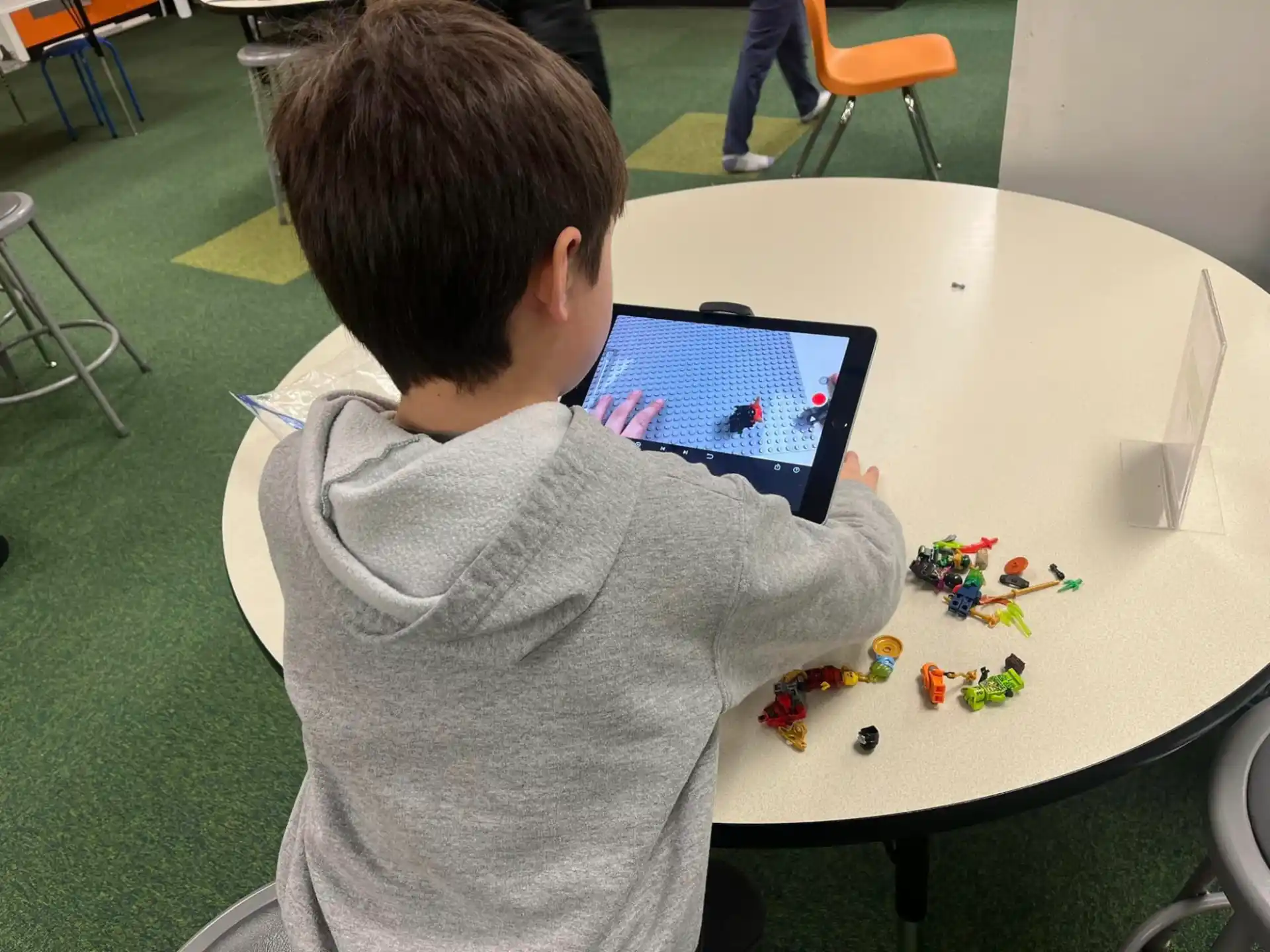 a boy sitting at a table with a tablet and toys on it