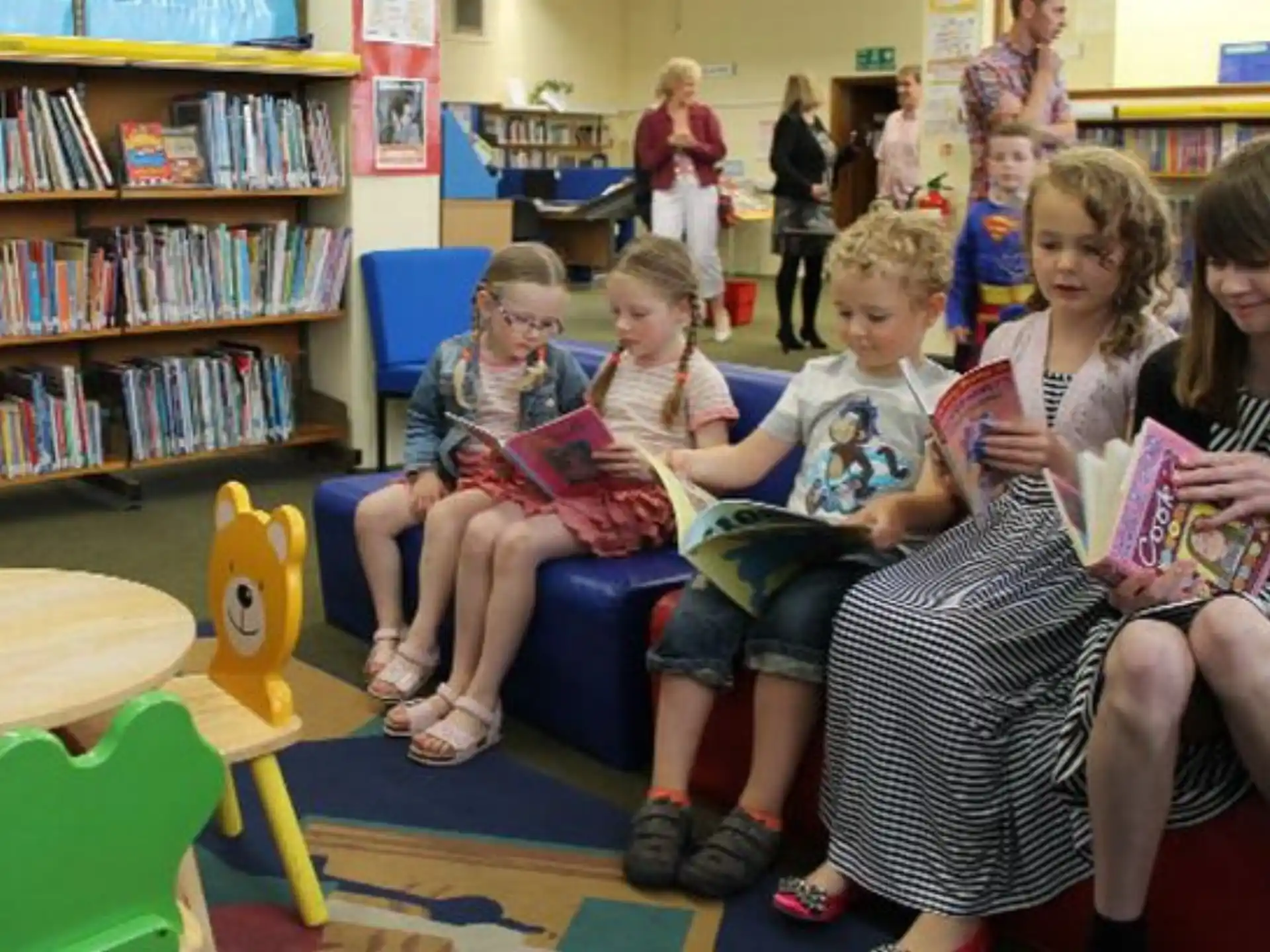 a group of children sitting on a couch reading books