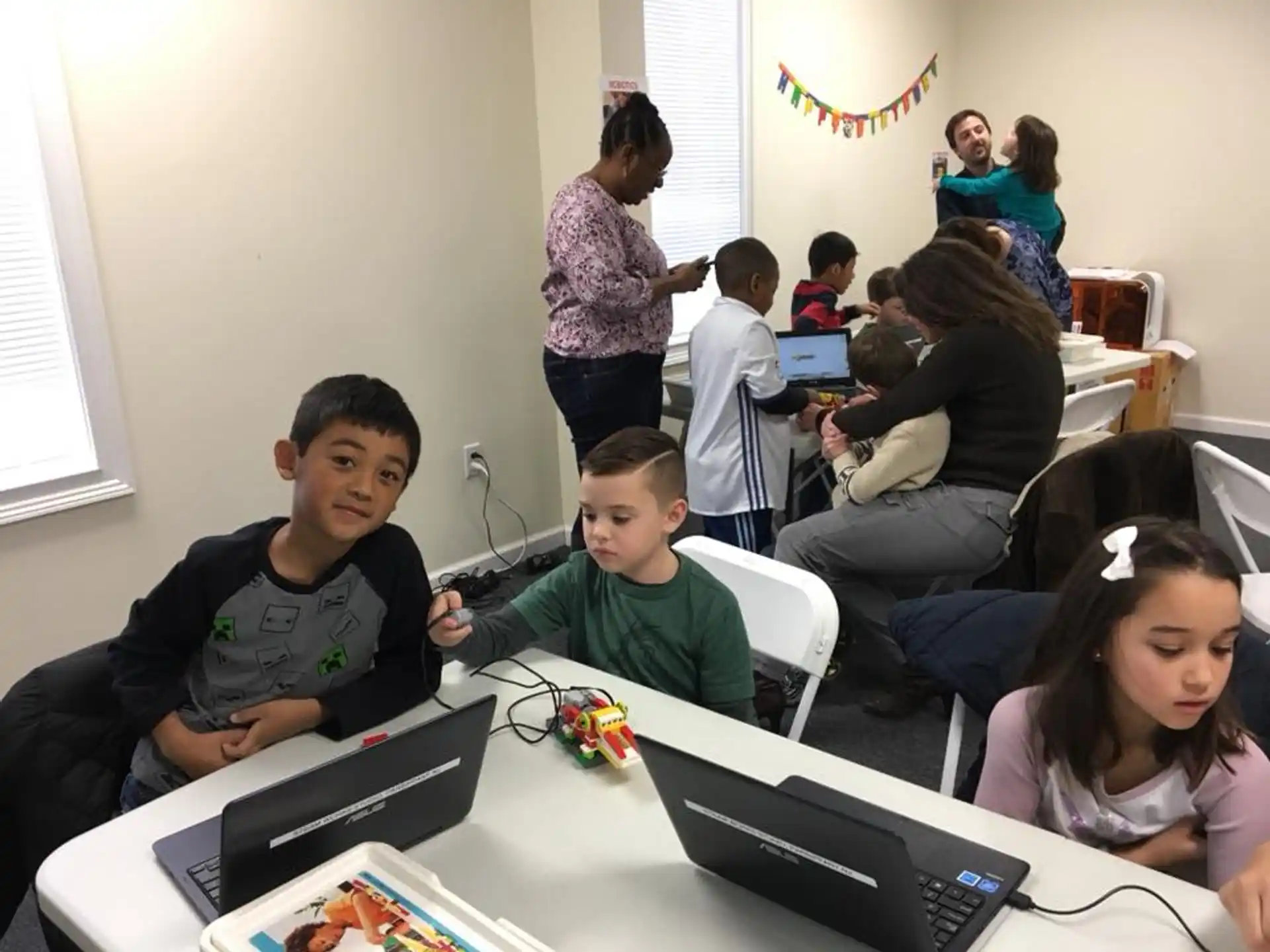 a group of children sitting at a table with laptops and toys