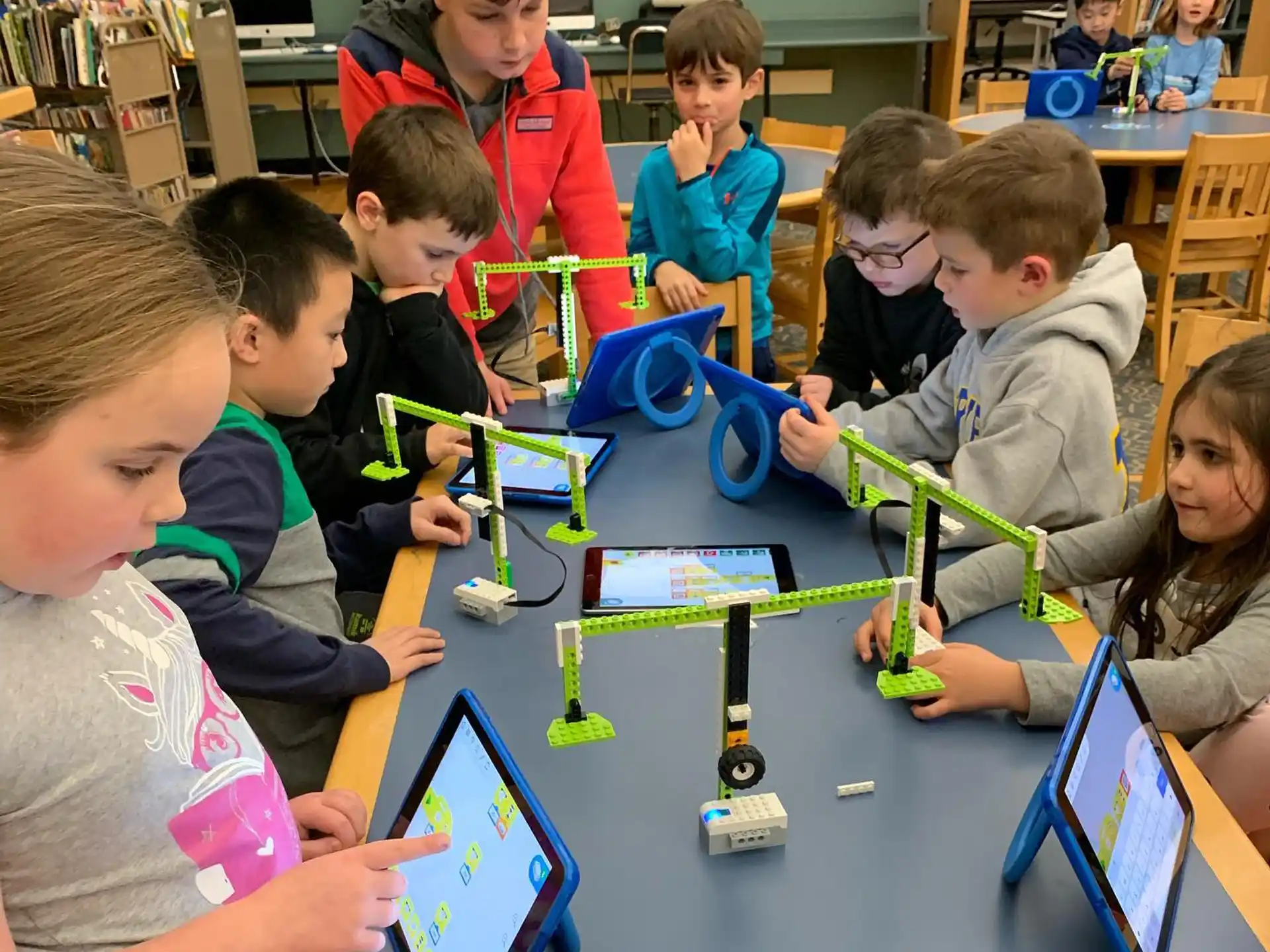 a group of children sitting at a table looking at a tablet