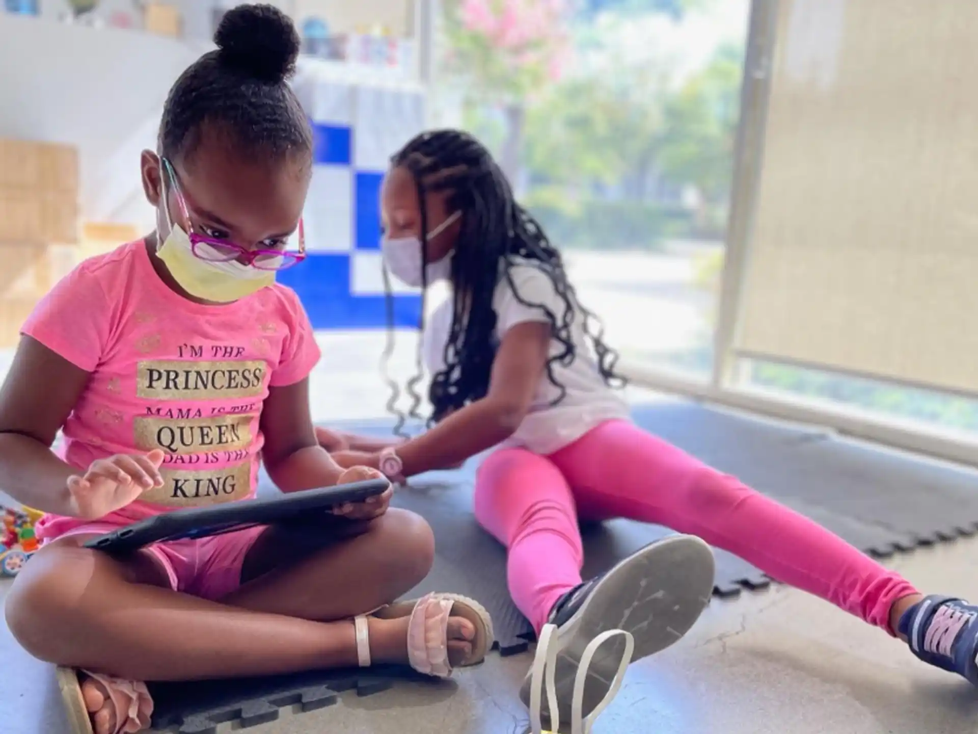 a couple of girls sitting on the floor looking at a tablet