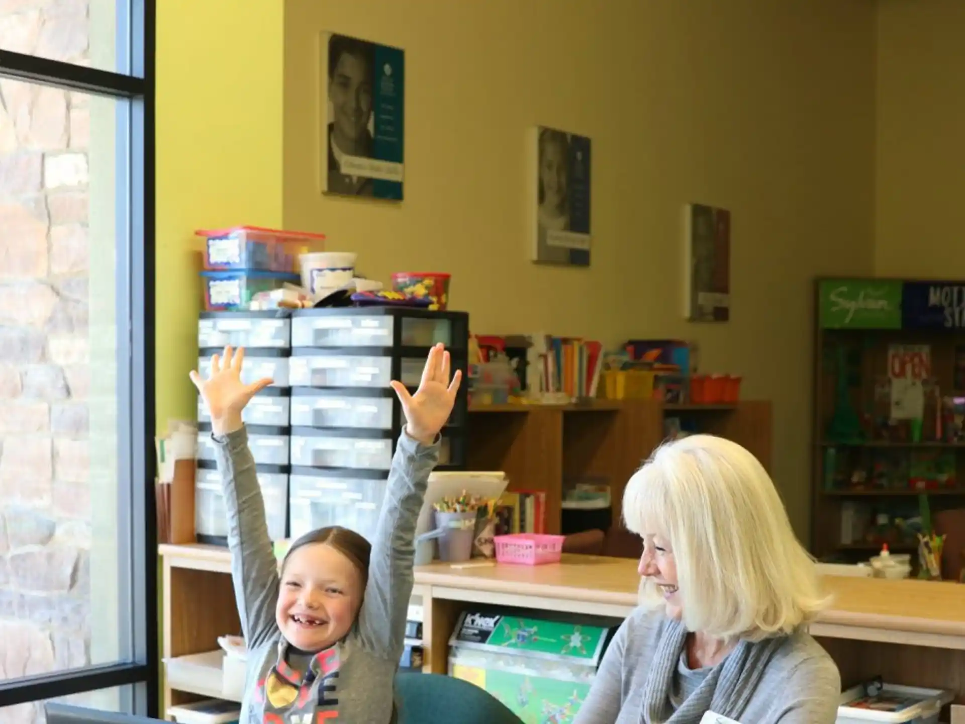 a person and a child raising their hands in a room with a window
