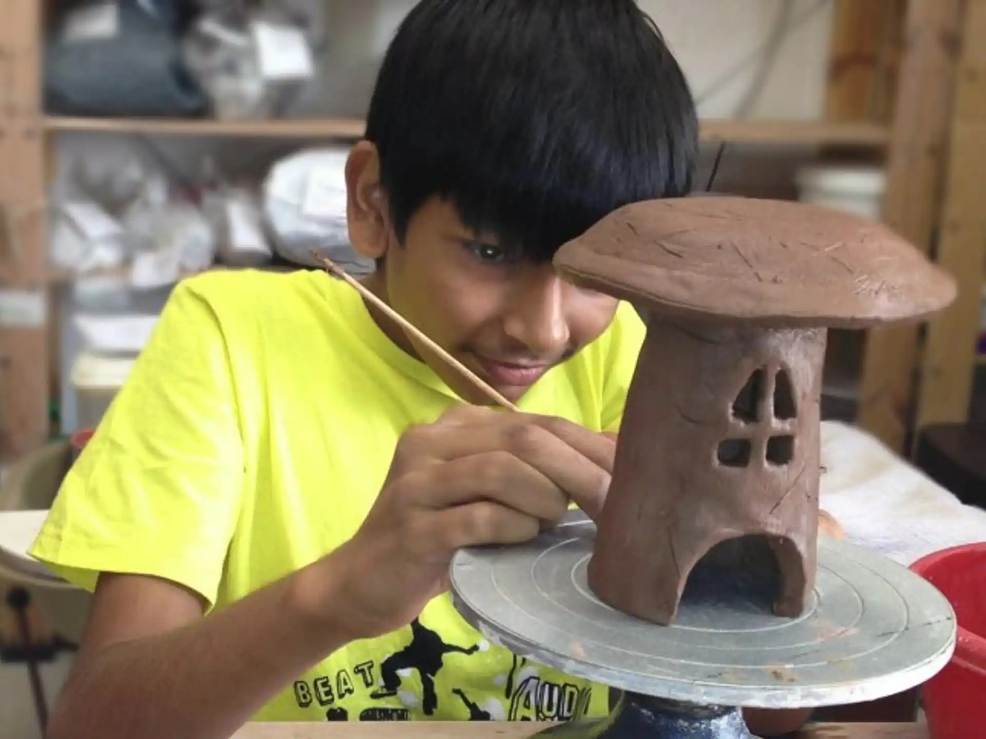 a young boy painting a clay pot