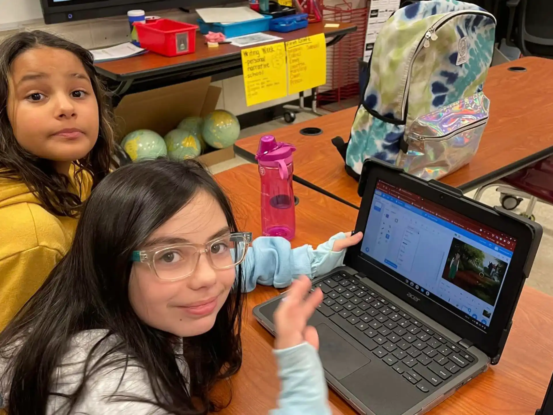 a couple of girls sitting at a table with a laptop