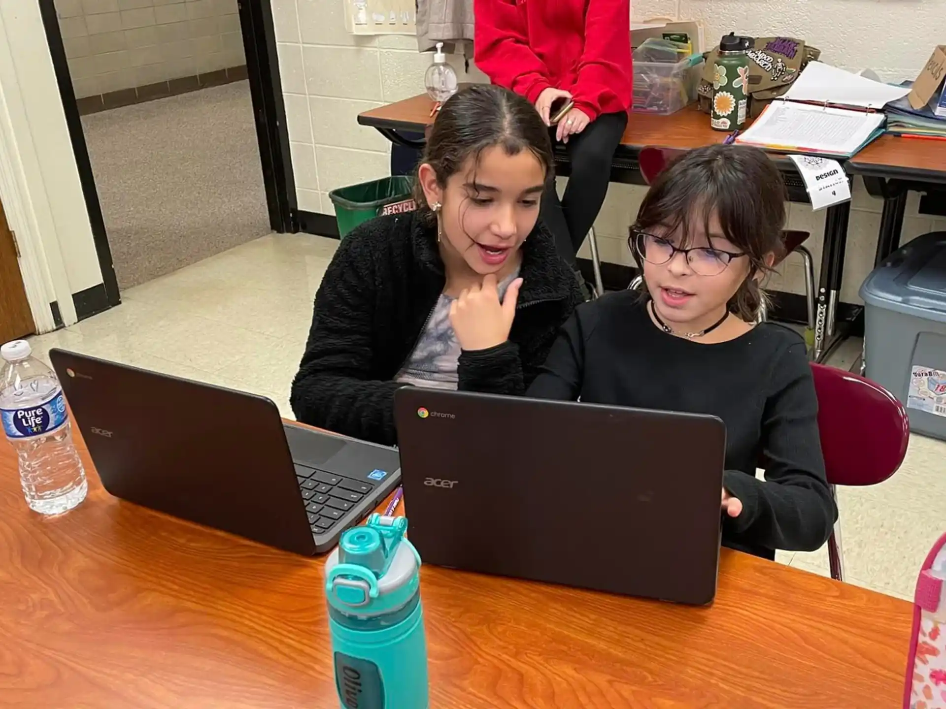 a couple of girls sitting at a table with laptops