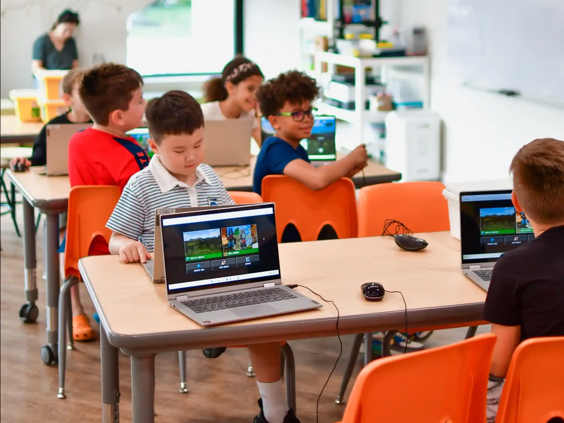a group of kids sitting at a table with laptops