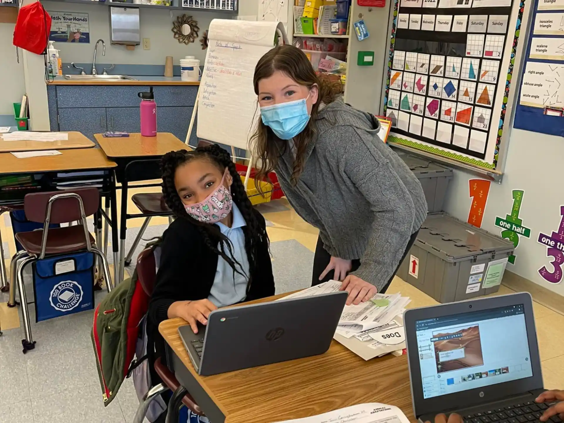 a couple of people wearing masks and sitting at a desk with a laptop