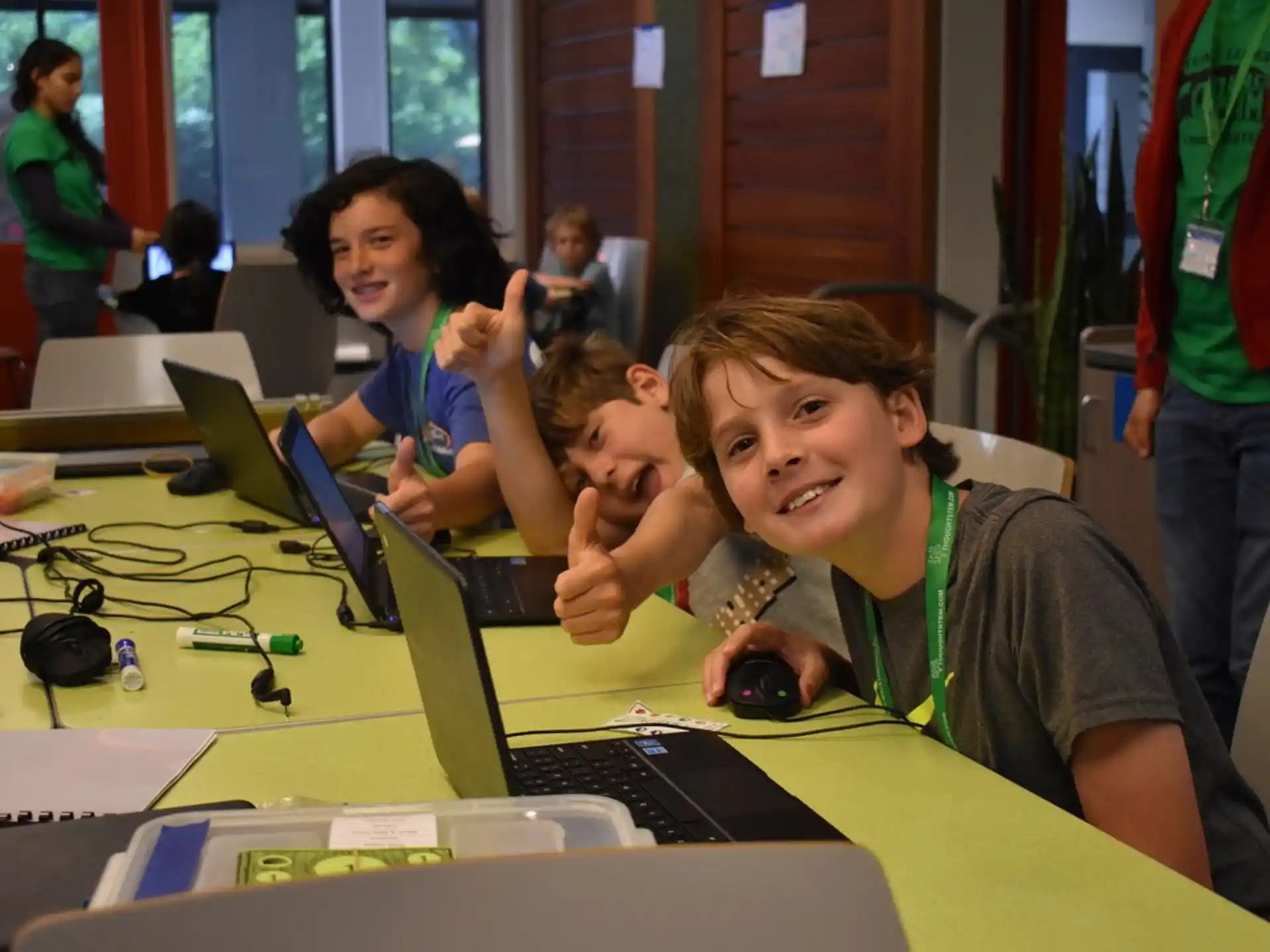 a group of kids sitting at a table with laptops