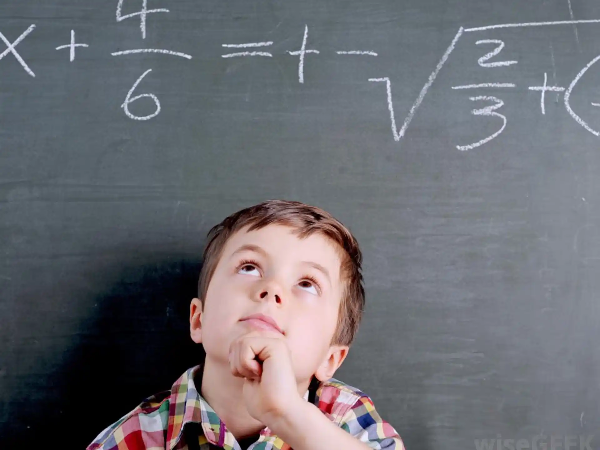 a boy with his hand on his chin in front of a chalkboard