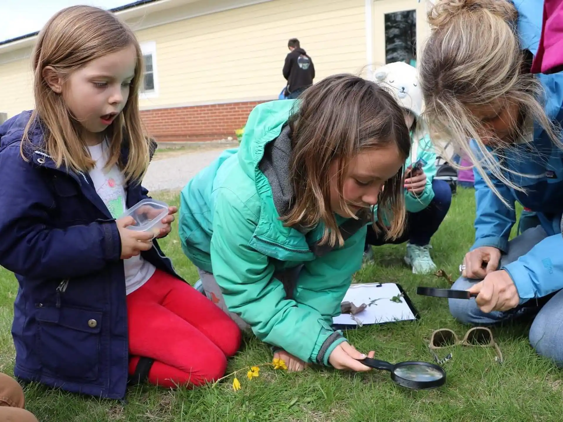a group of girls sitting on the grass looking at a piece of paper