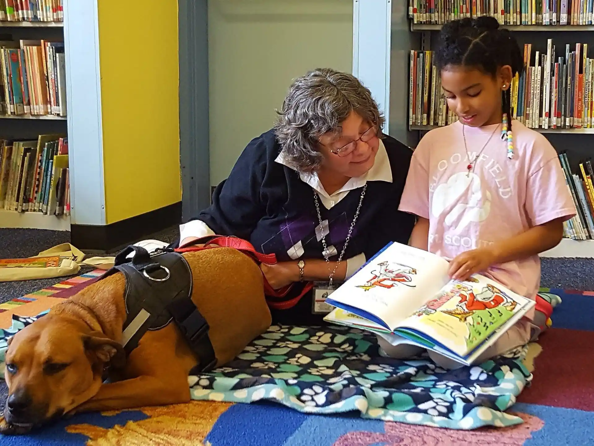 a person and a dog reading a book to a girl