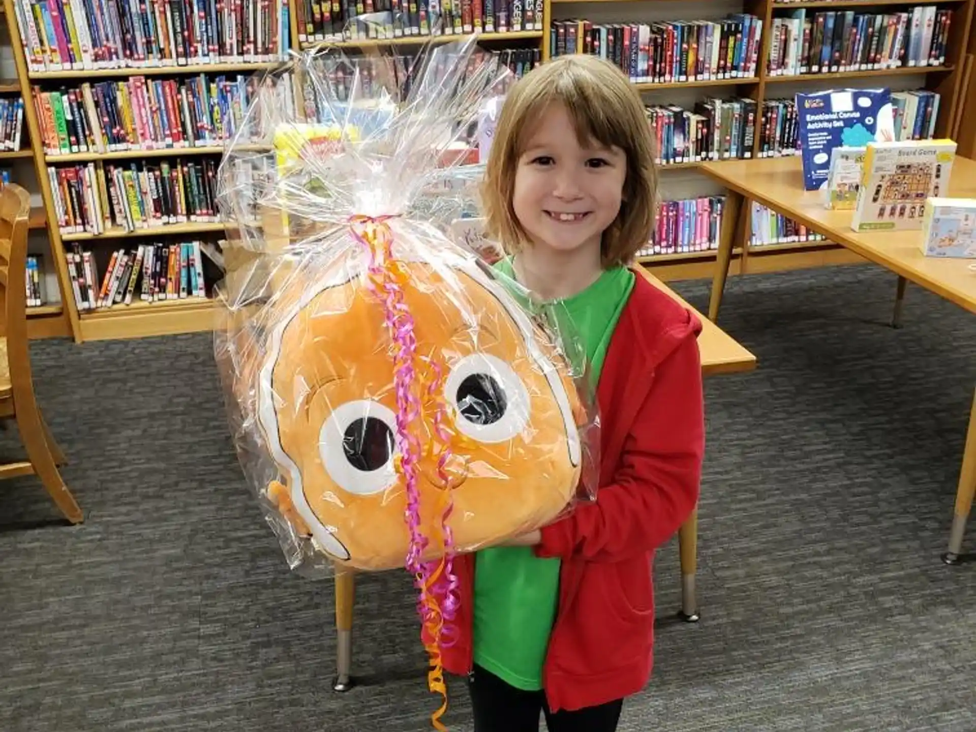 a girl holding a large yellow and red object in a library