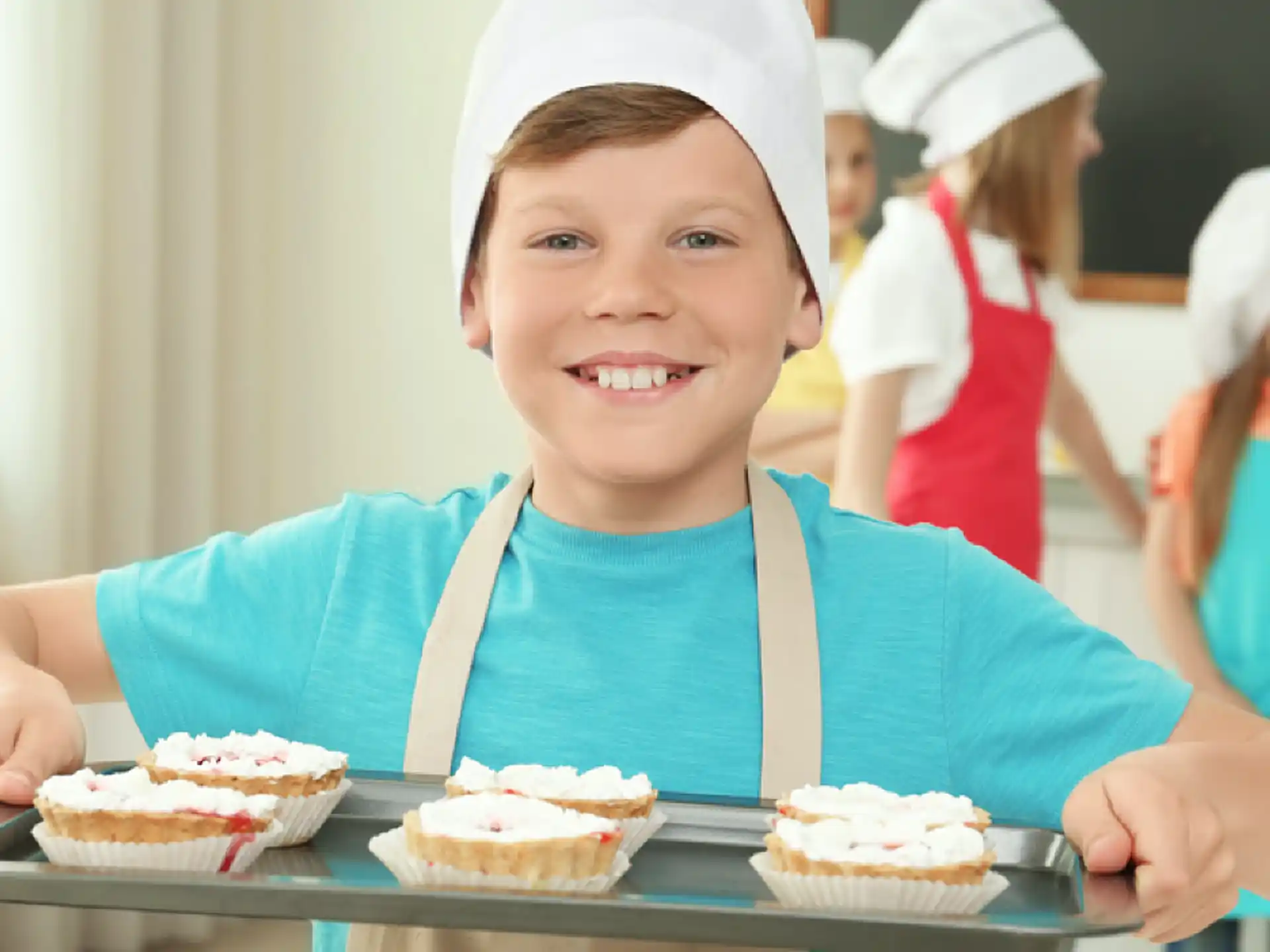 a boy smiling with a tray of cupcakes