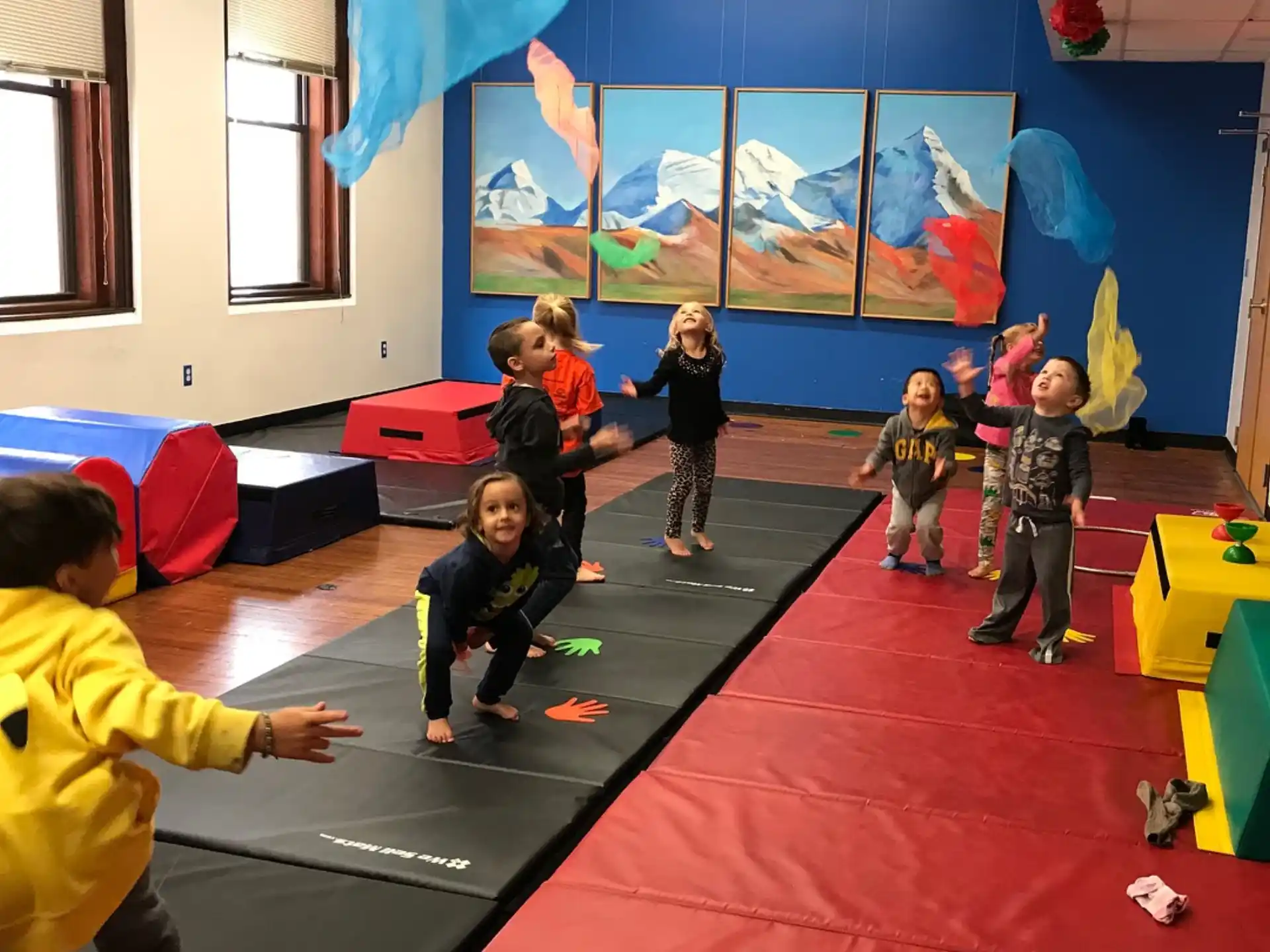 a group of children playing on a red carpet in a room with a large screen
