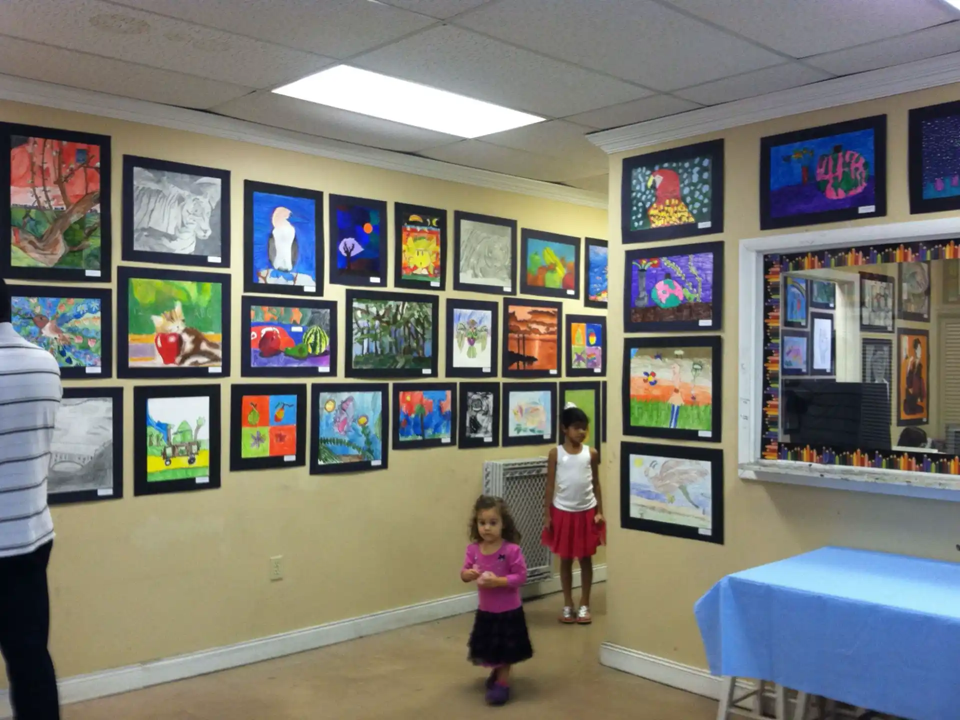 a couple of children standing in a room with a wall of art