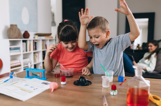 a couple of children sitting at a table with their hands up