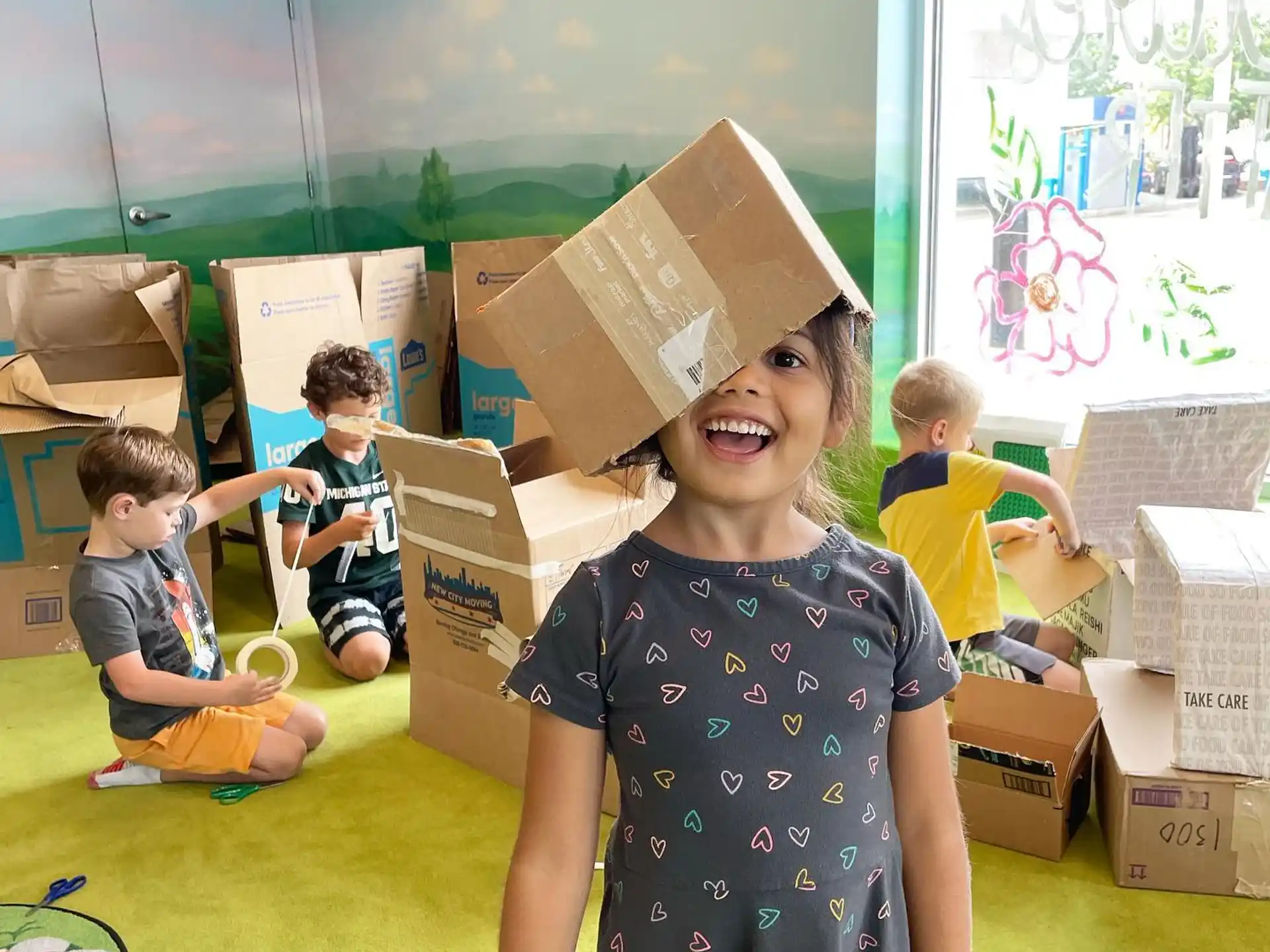 a group of children in a room with boxes and a girl in a dress